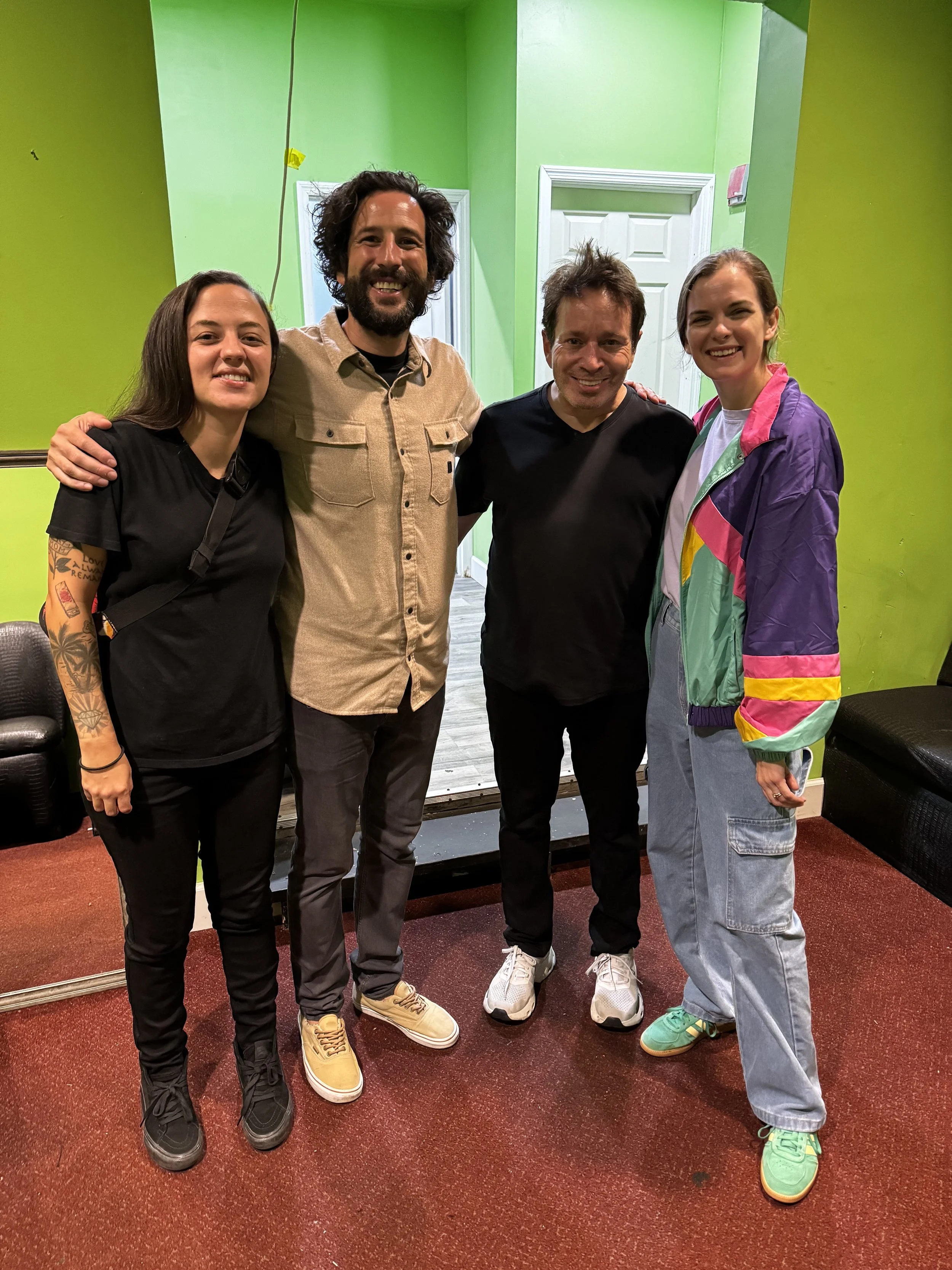 Four people standing together indoors, smiling, with a green wall and white door in the background.