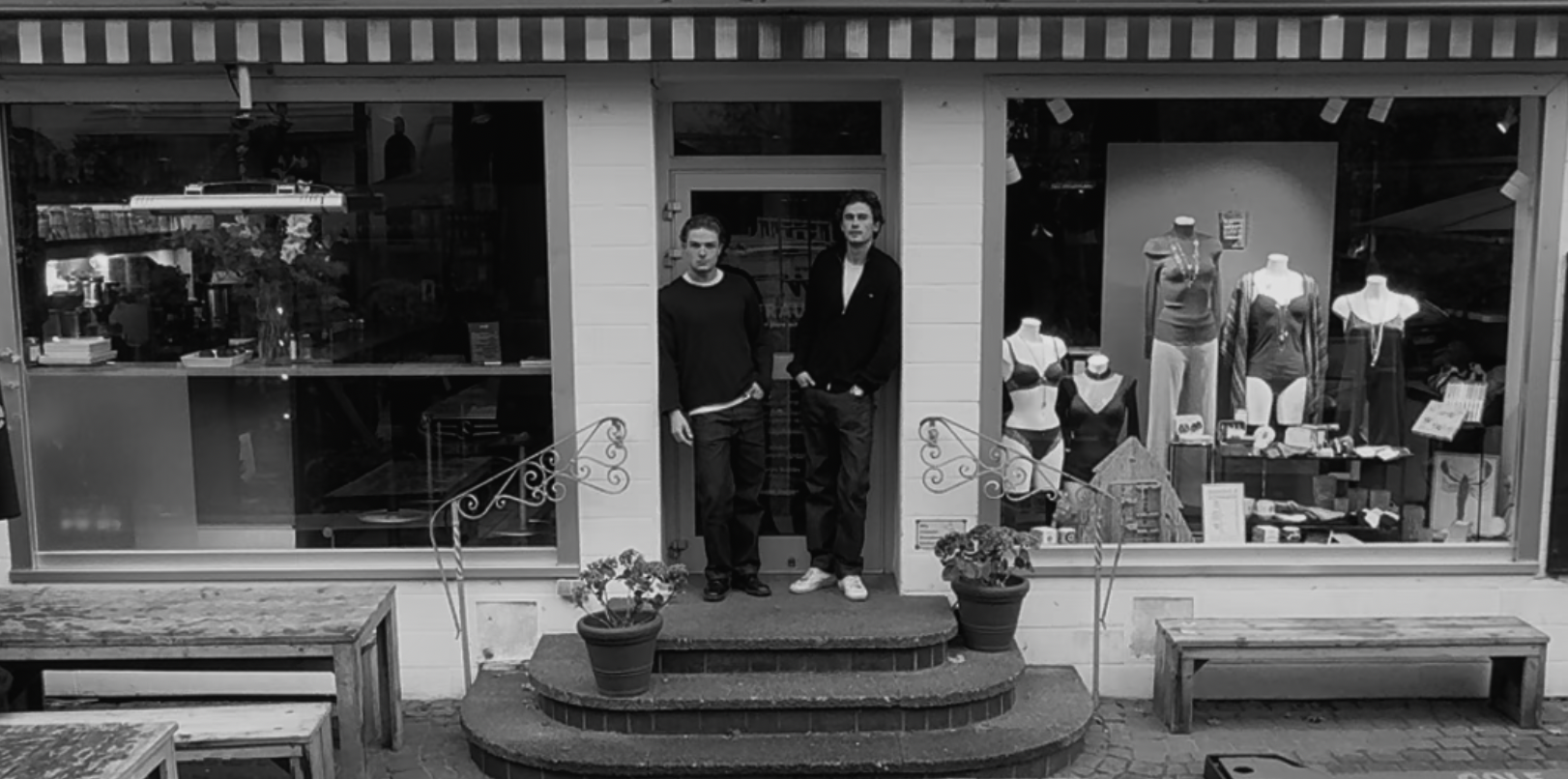 Zwei junge Männer stehen auf den Treppen vor einem Schaufenster eines Kleidungsgeschäfts.