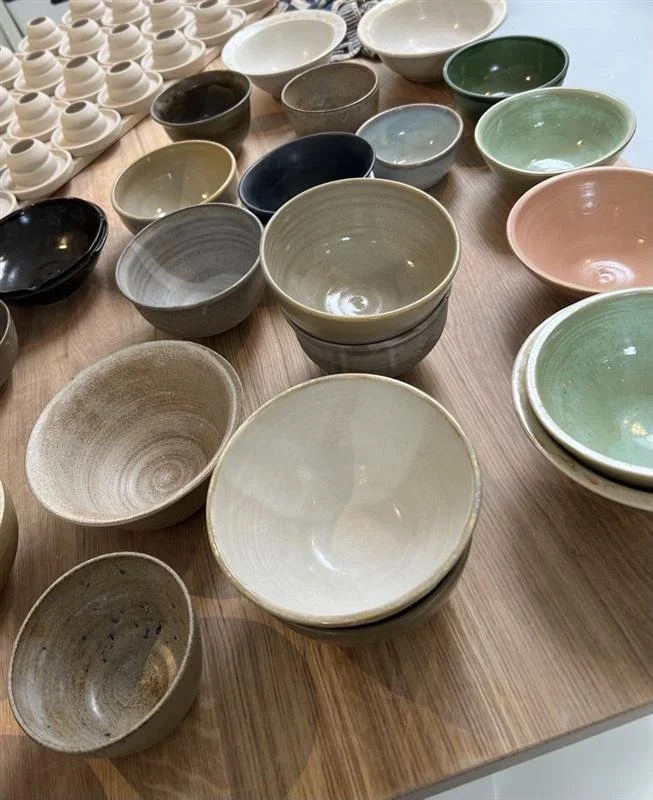 Various ceramic bowls and cups in different sizes and colors on a wooden table.