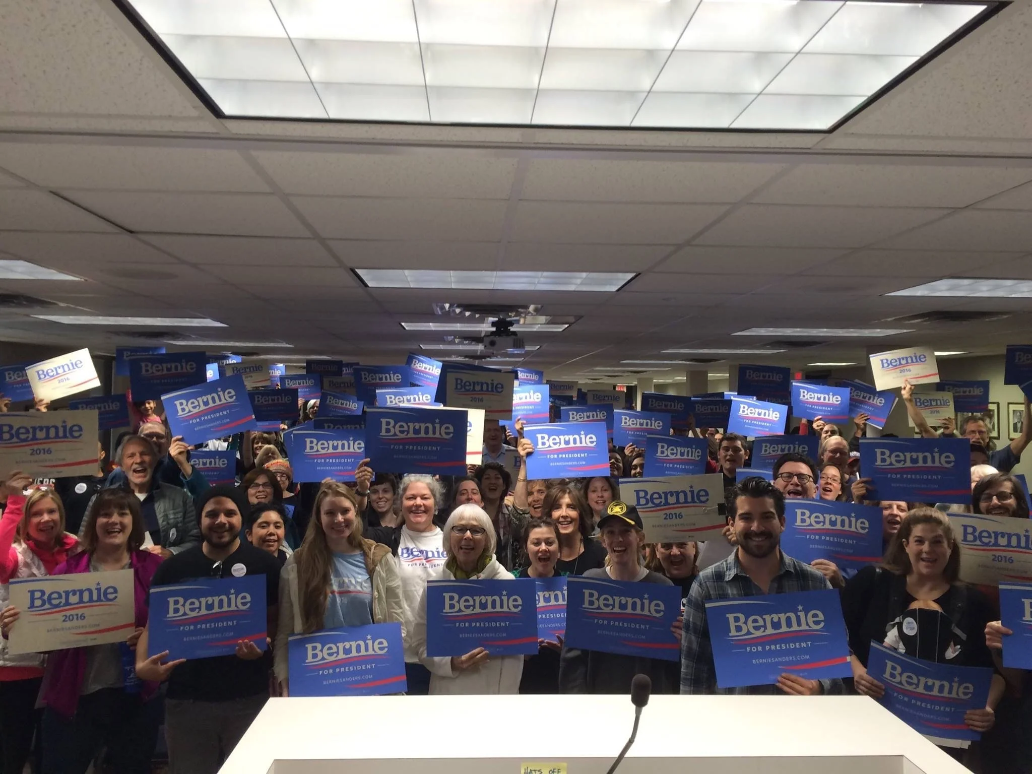 Crowd of people with Santiago Palomino holding Bernie Sanders 2016 campaign signs at a rally or event.