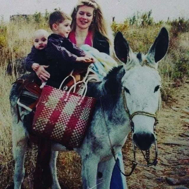 Santiago Palomino and his mother riding a donkey with two children, one in front and one in her arms, in an outdoor field.
