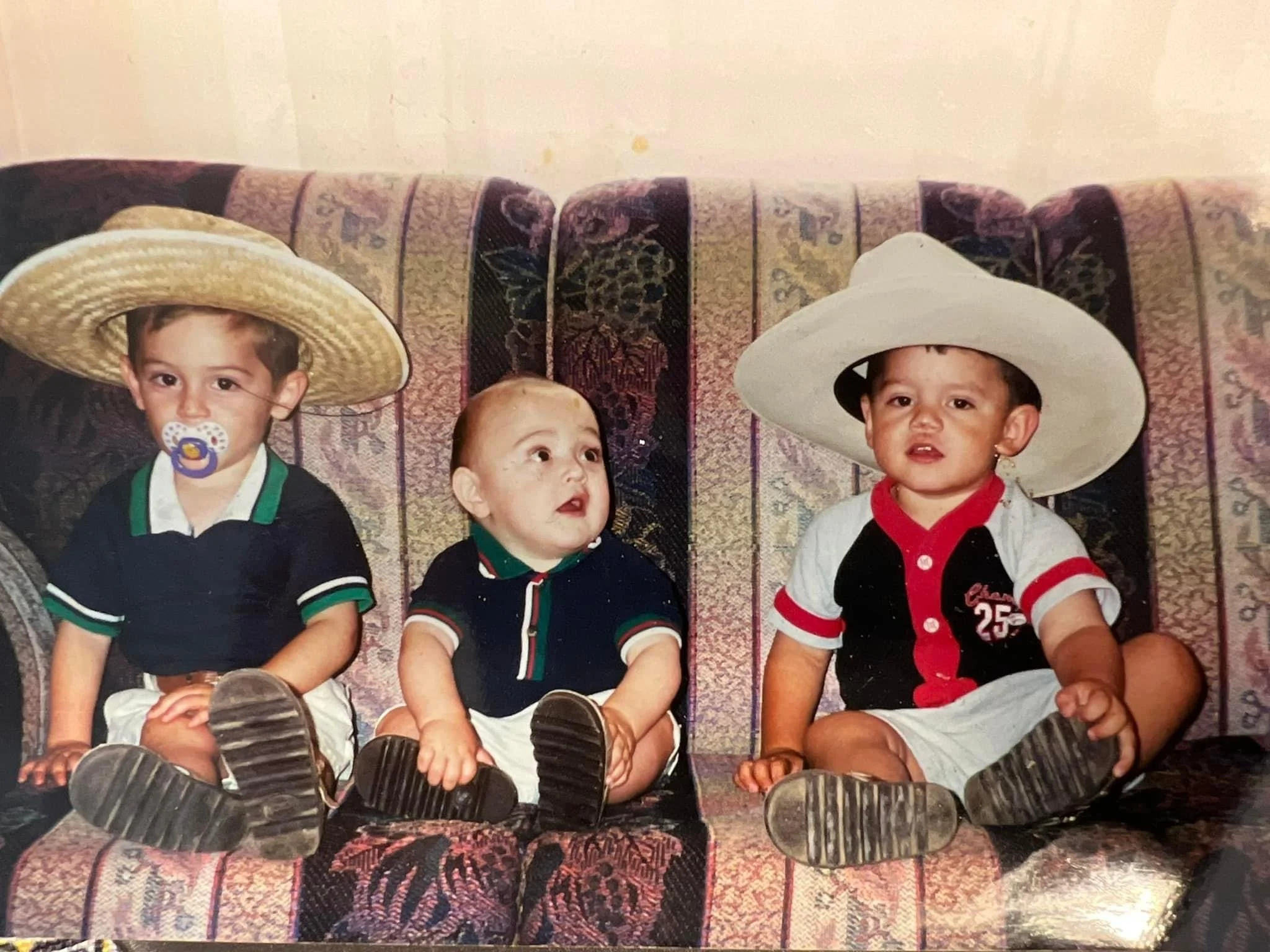Santiago Palomino and his brothers as children sitting on a patterned couch, wearing sombreros, cowboy hats, and casual clothing.