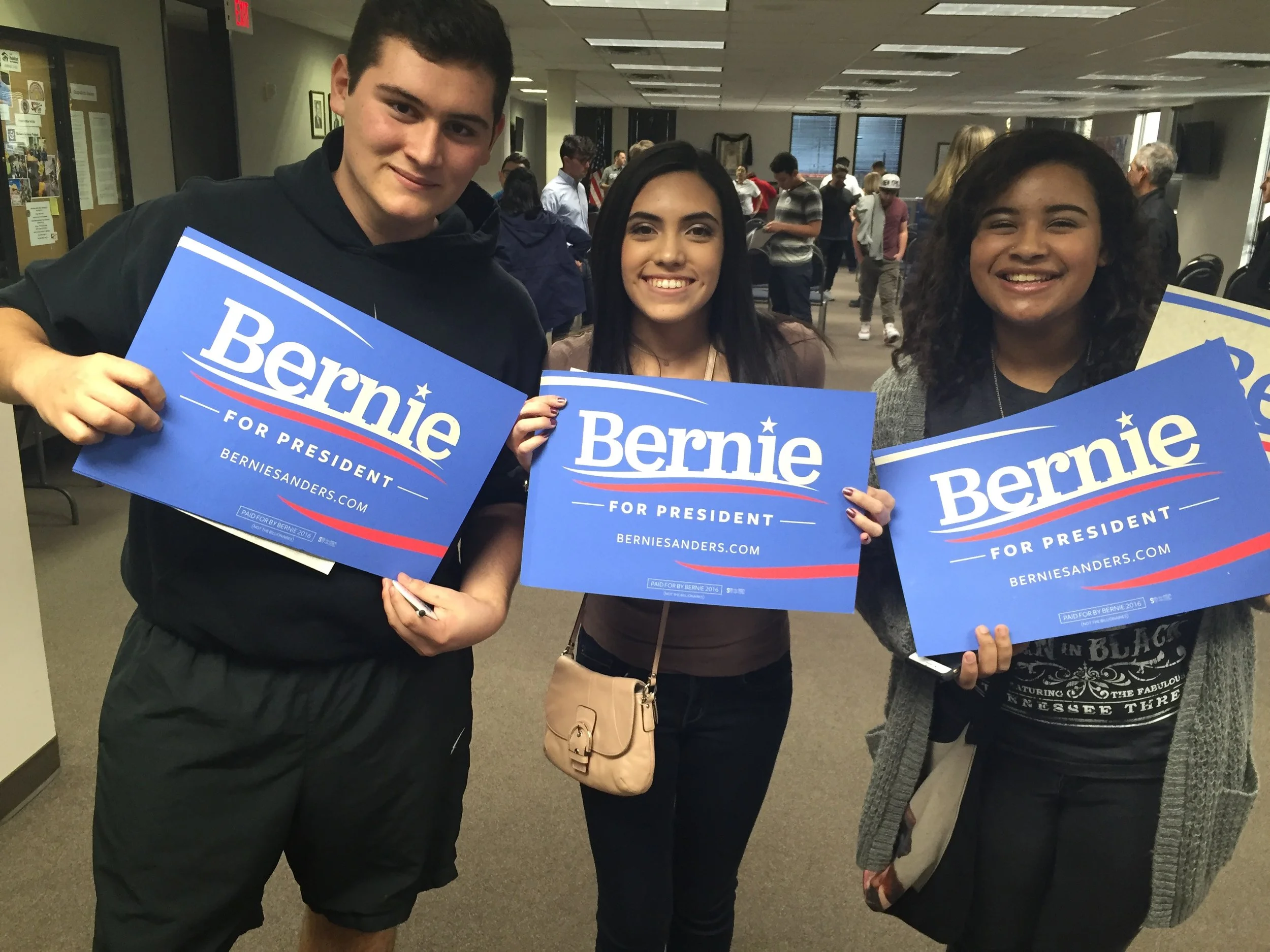 Santiago Palomino and two young people holding Bernie Sanders for President signs at a gathering.