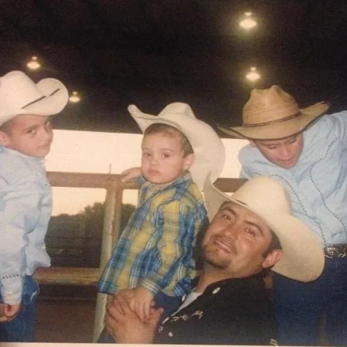 Santiago Palomino and his brothers and father wearing cowboy hats, indoors with a wooden railing and trees outside the window.