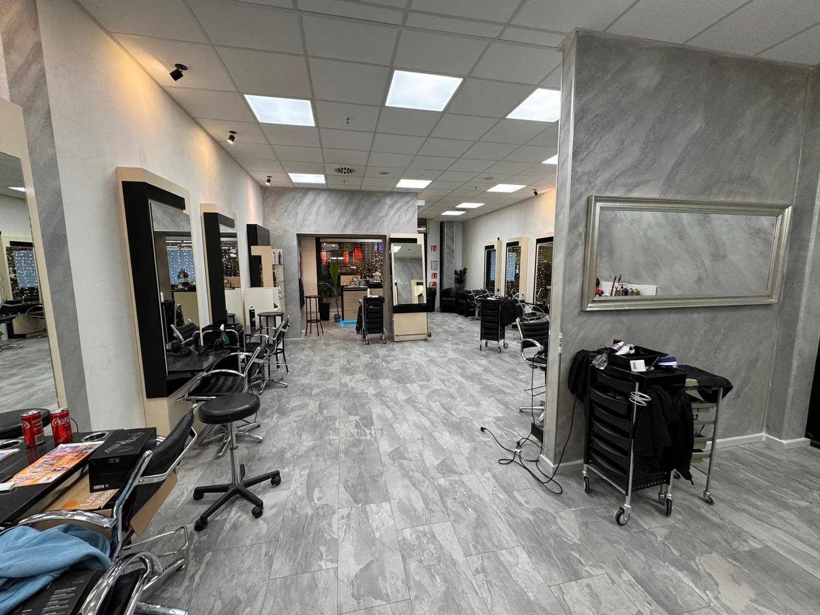 Ein Friseursalon mit Waschtischen, Styling-Arbeitsplätzen, Spiegeln und Friseurstühlen, sowie einem Rollwagen mit Friseurzubehör.