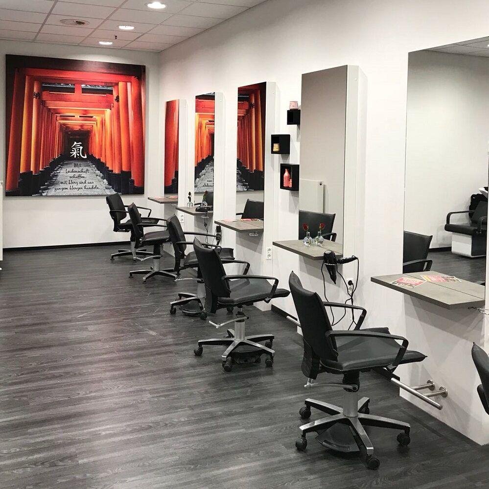 Ein Friseursalon mit mehreren schwarzen Stylingstühlen vor Waschtischen und großen Wandbildern mit roten Torii-Toren in Japan.