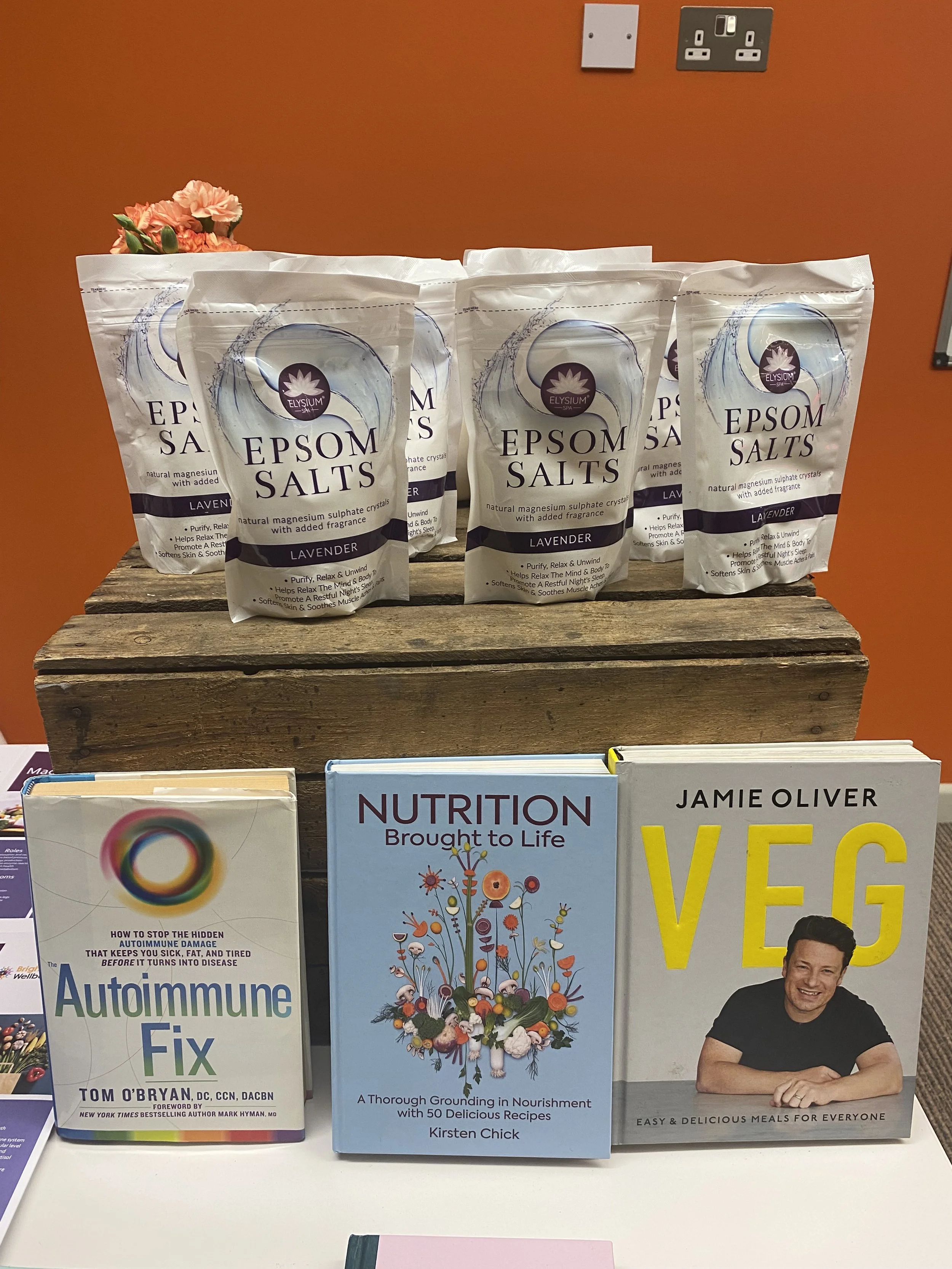 Epsom salts lavender scent in white packaging, three bags on a wooden stand, books about autoimmune health, nutrition, and vegetarian recipes displayed in front.