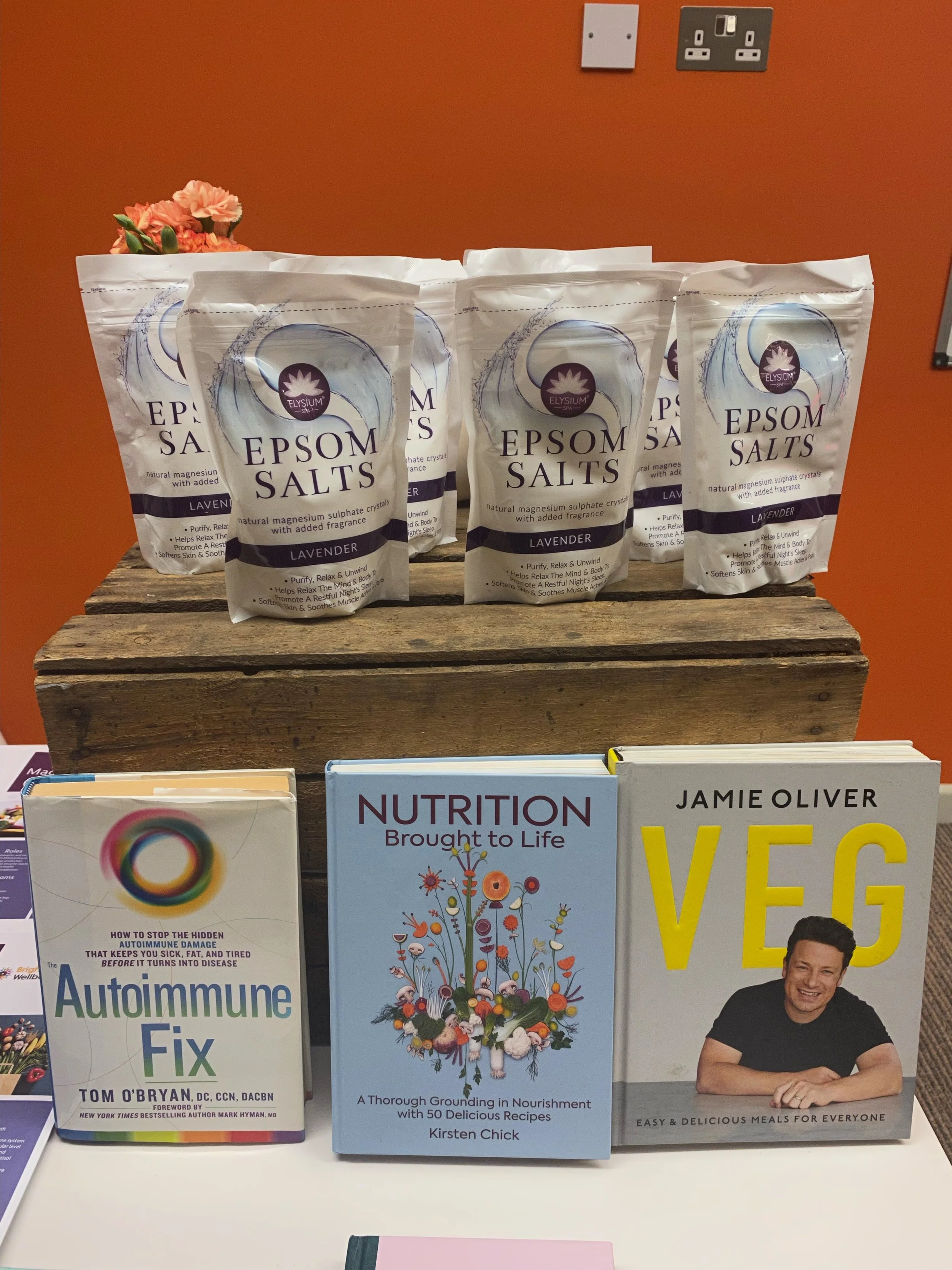 Four packs of Epsom salts lavender fragrance on a wooden surface, with three books about health, nutrition, and vegan cooking in front.