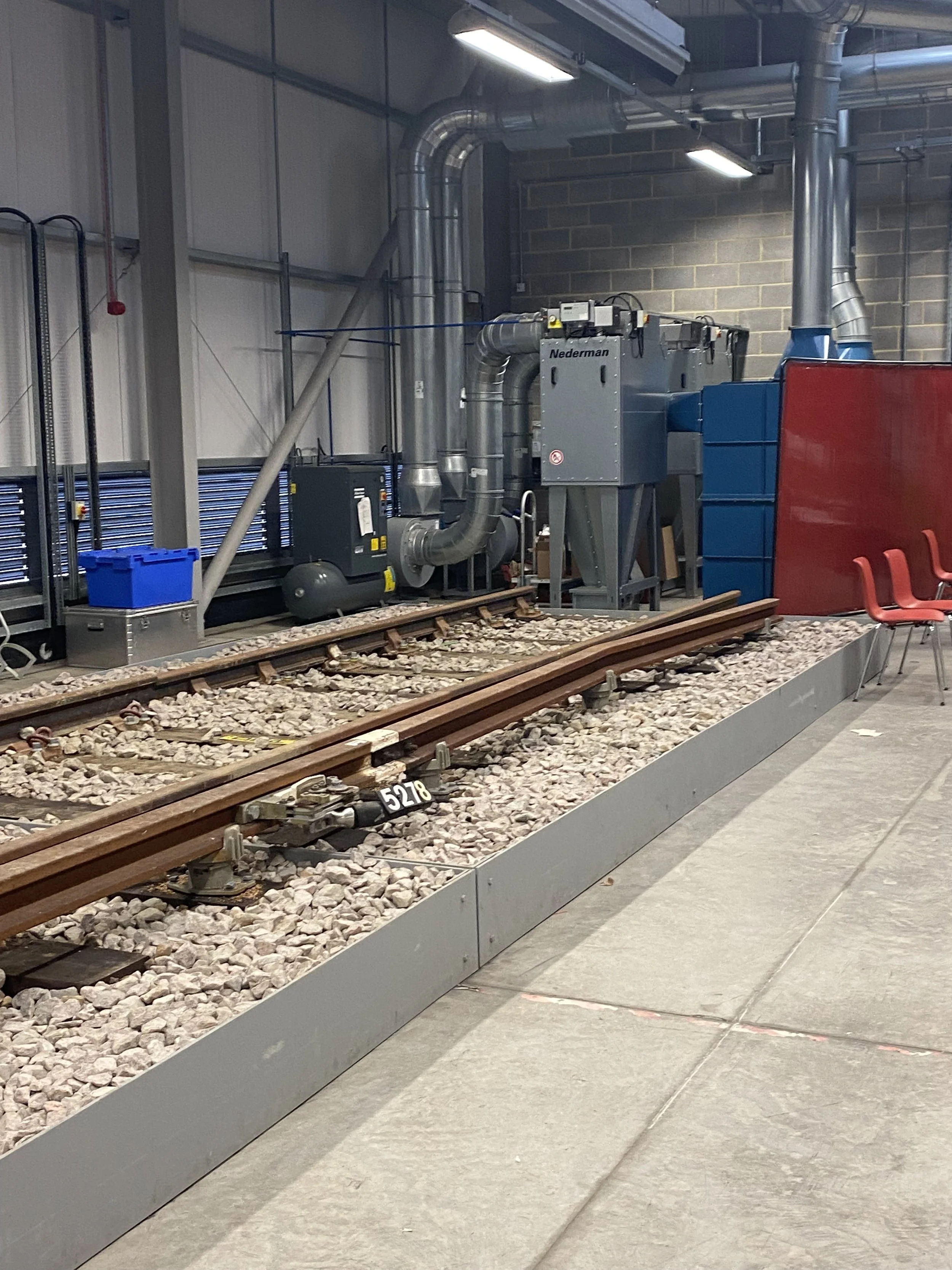 Indoor railway track display with a section of railroad track and related machinery, chairs are placed nearby.