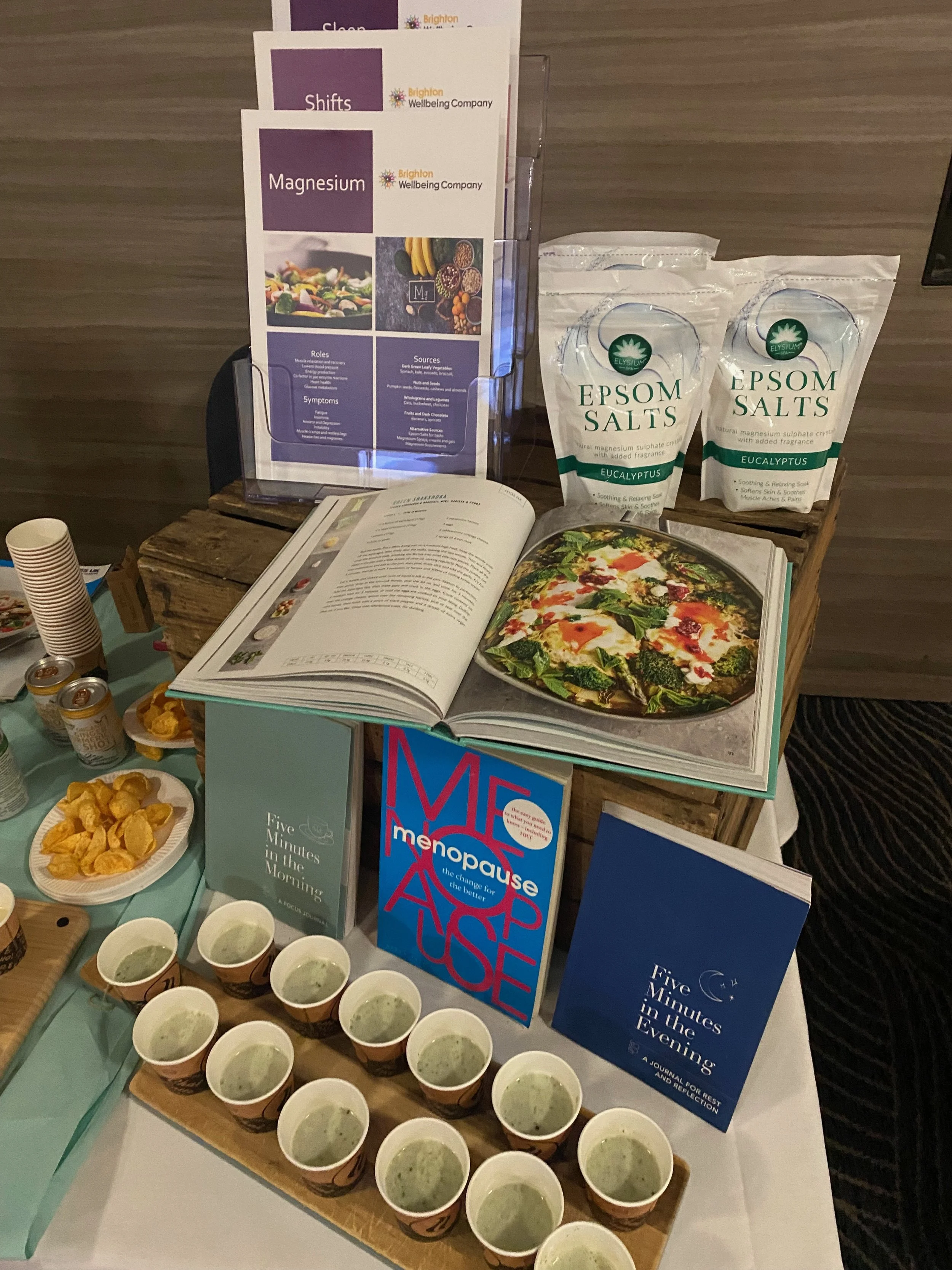 Display table with books, Epsom salts, spinach dip, and tea cups. Informational cards about magnesium and health benefits. 