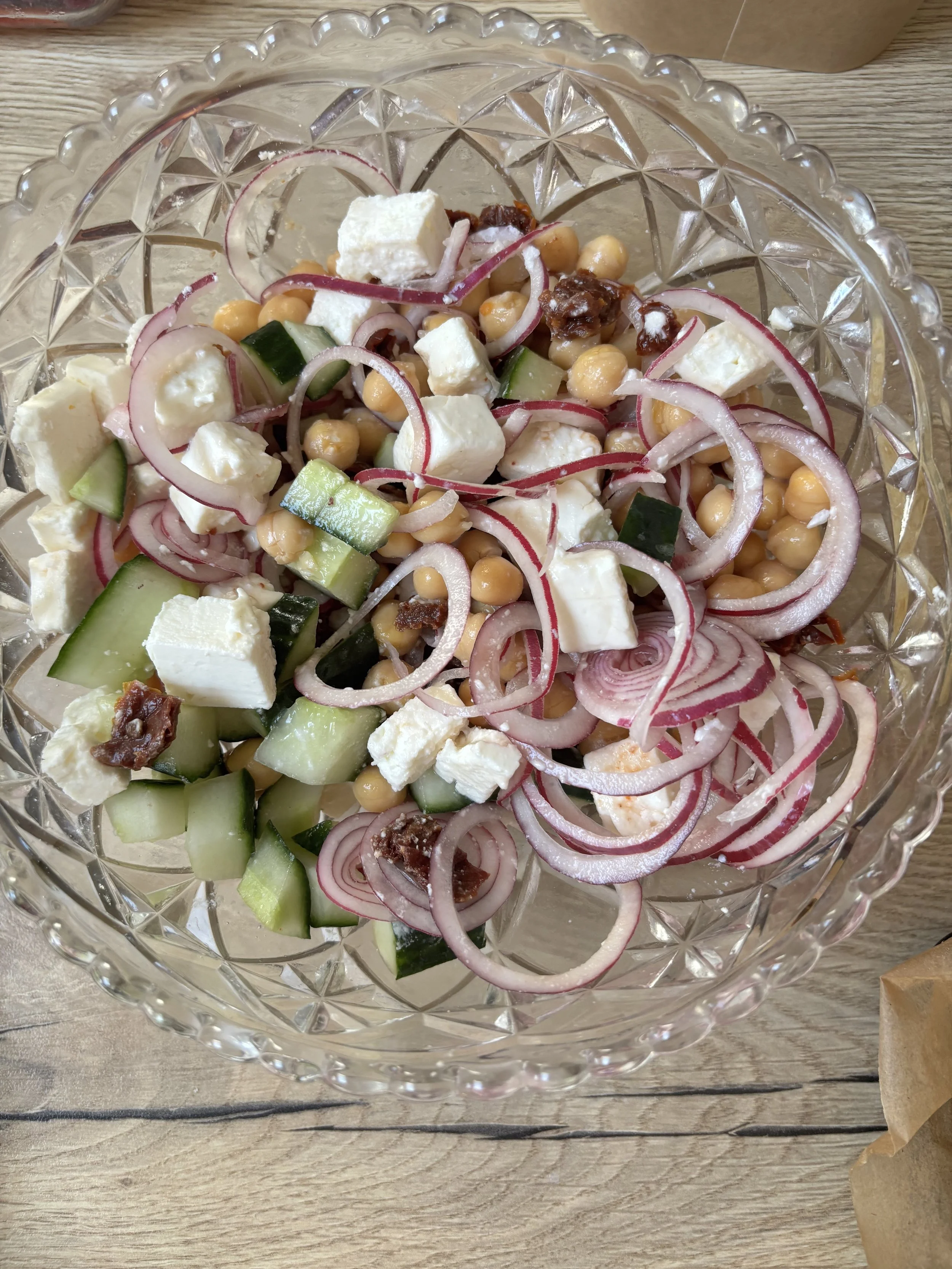 Cucumber, chickpeas, feta cheese, red onion, and sun-dried tomatoes in a glass bowl.