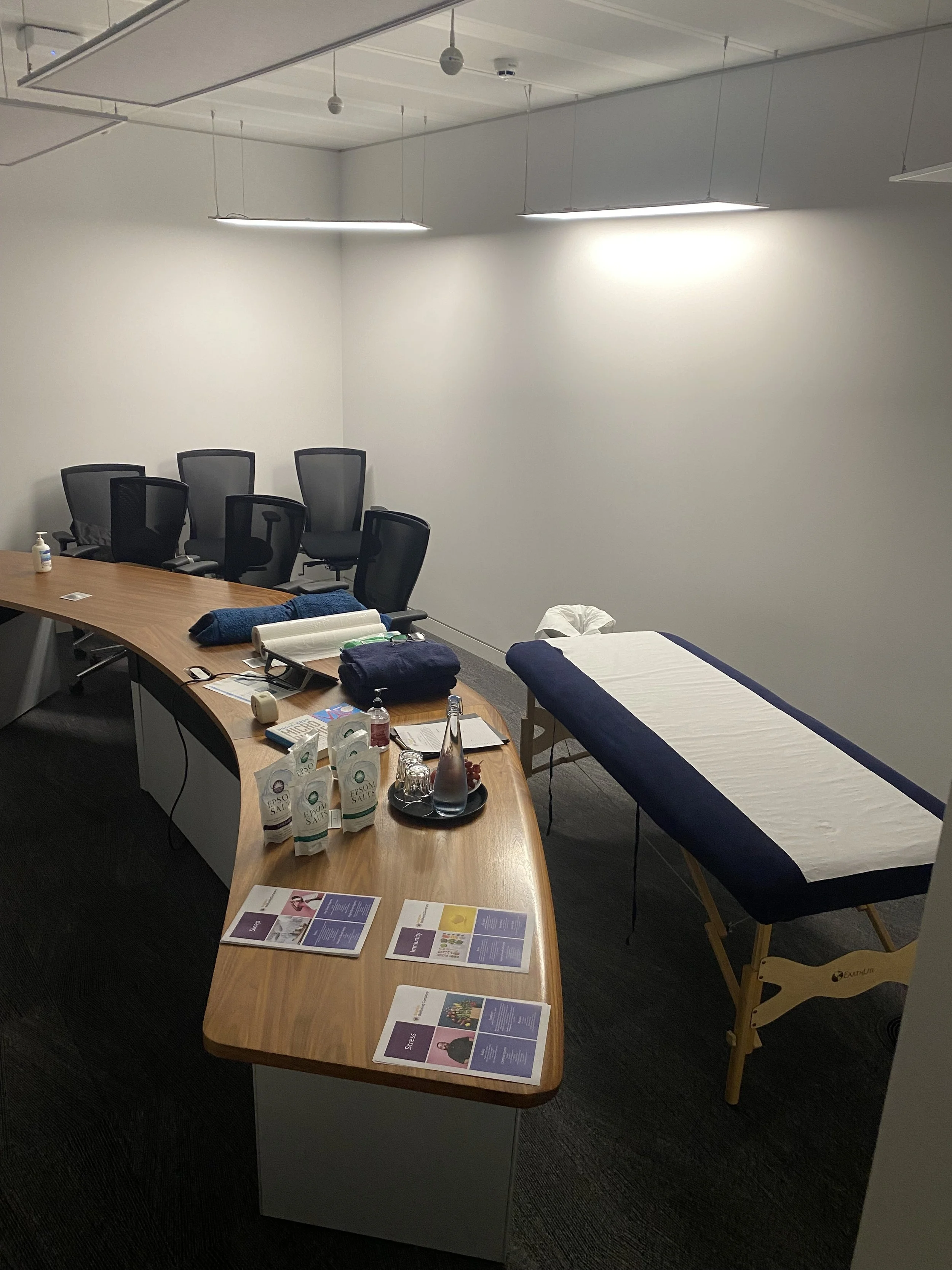 Conference room with a massage table, chairs, and various wellness products on the table.