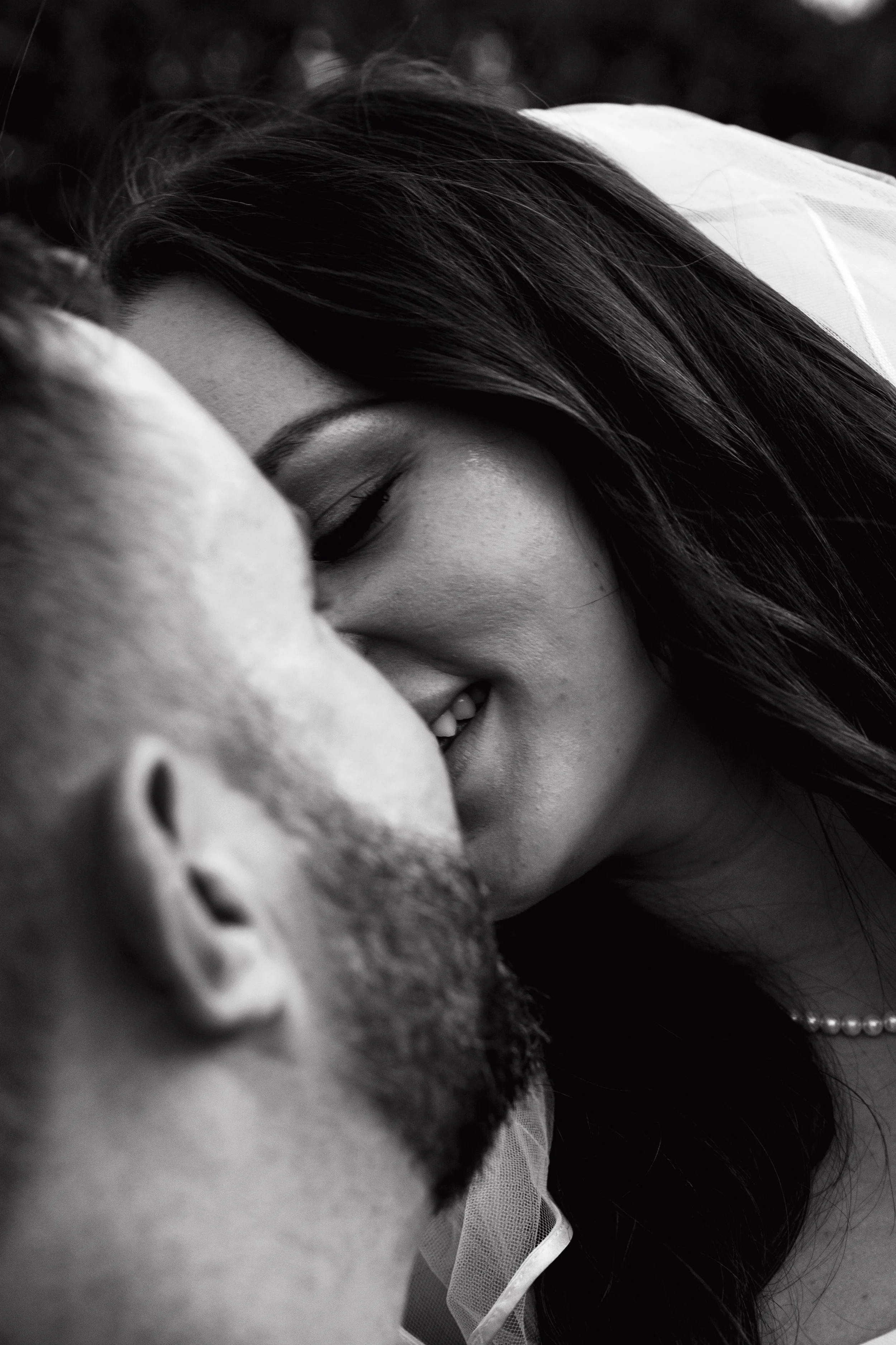 A black-and-white close-up photograph of a couple kissing, with the woman smiling and eyes closed, and the man's face partially visible.