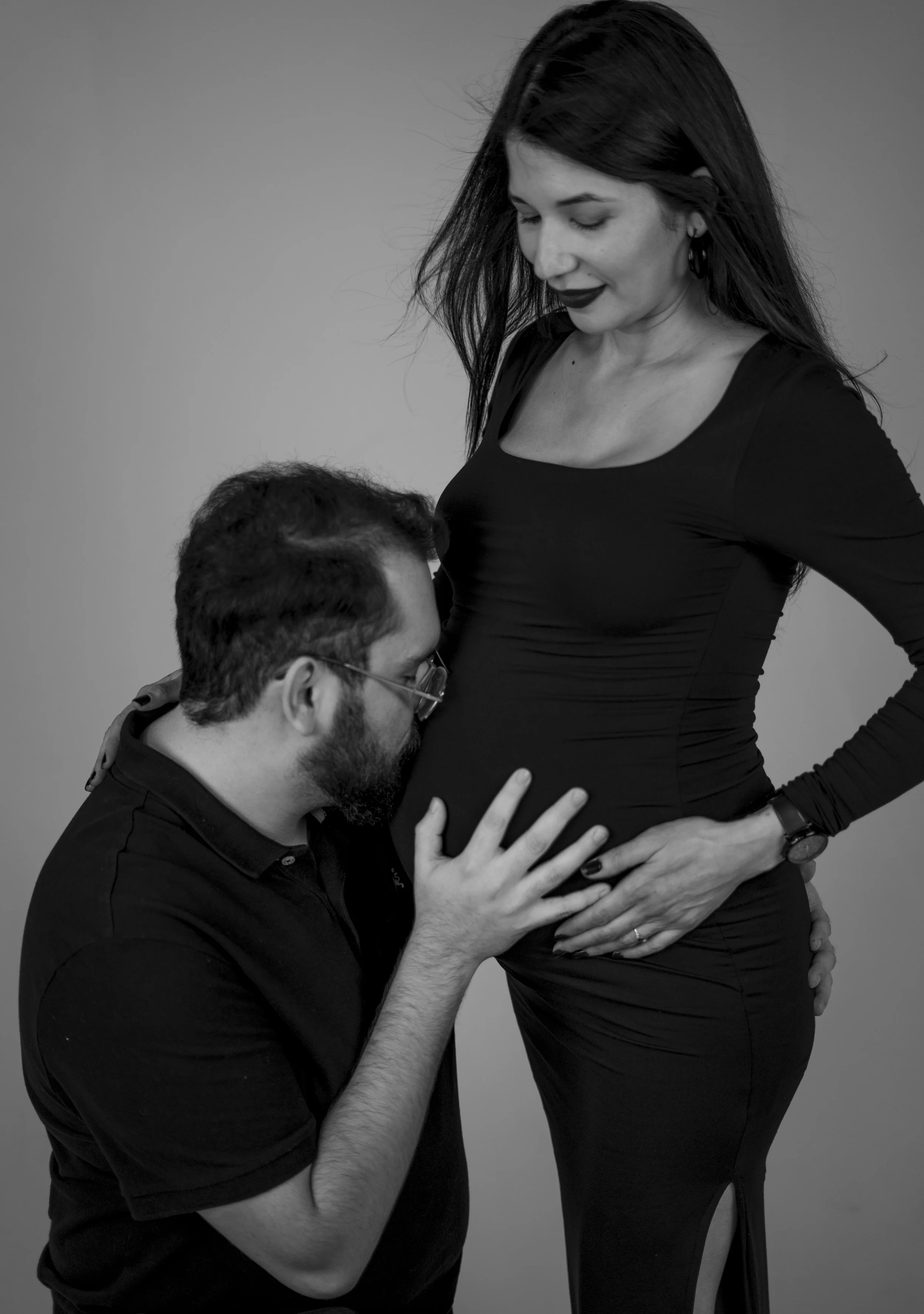 A man kneeling and kissing a pregnant woman's belly.