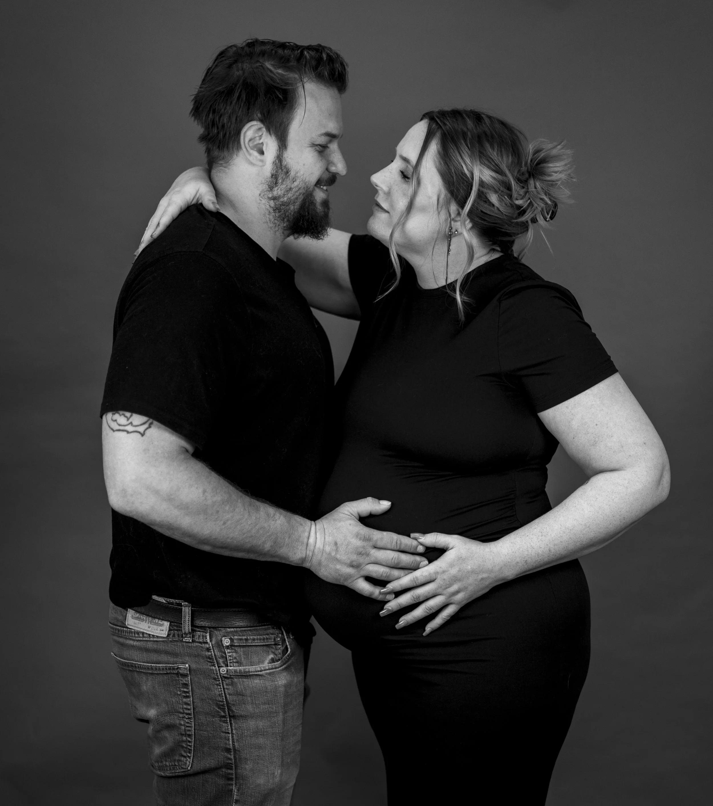 A black-and-white photo of a couple facing each other closely, with their foreheads almost touching, smiling, and tenderly holding each other.