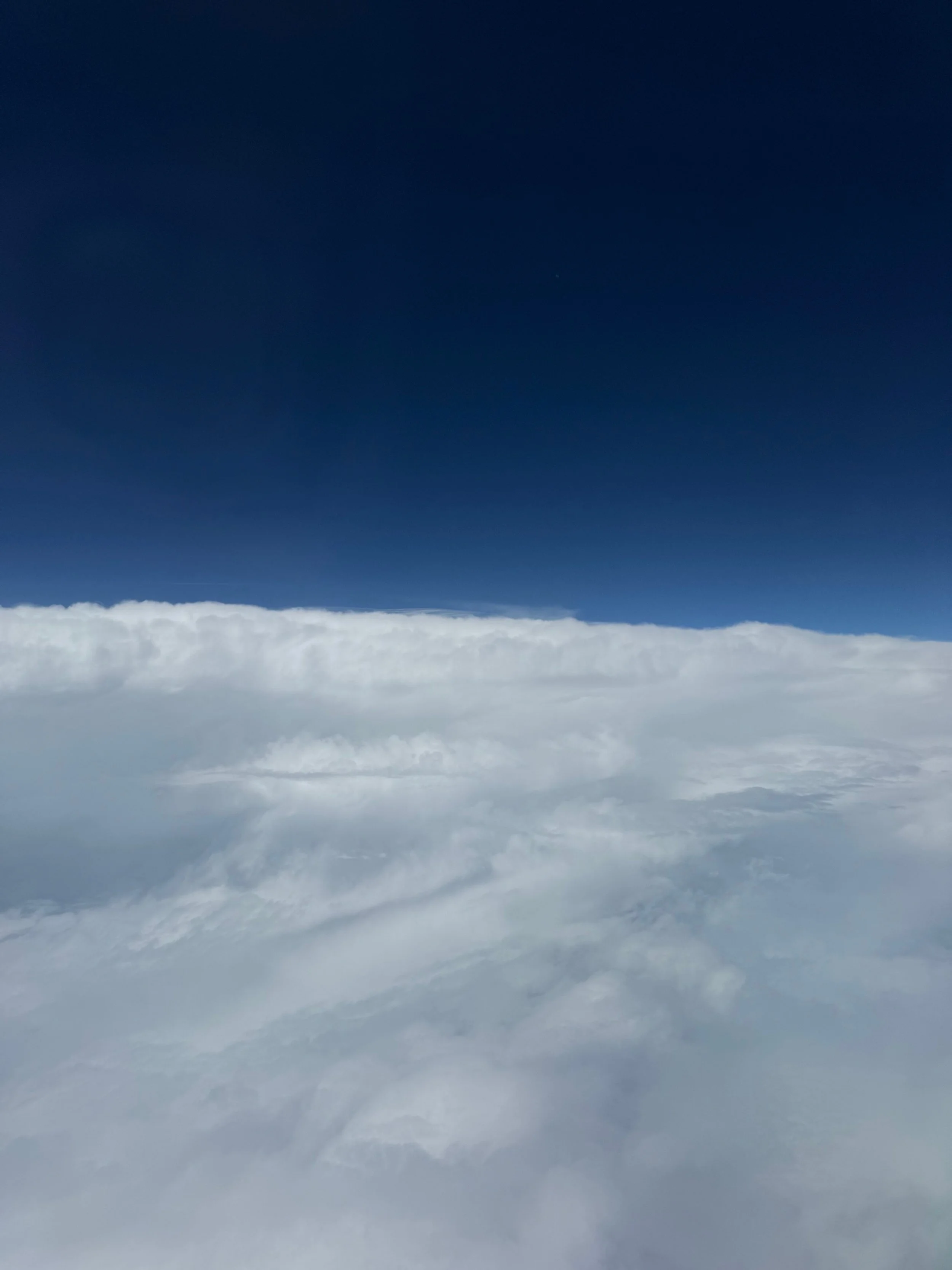 View from airplane window flying over clouds into dark blue sky