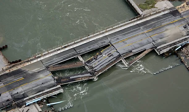 A damaged bridge over a body of water, with parts of the roadway collapsed and broken.