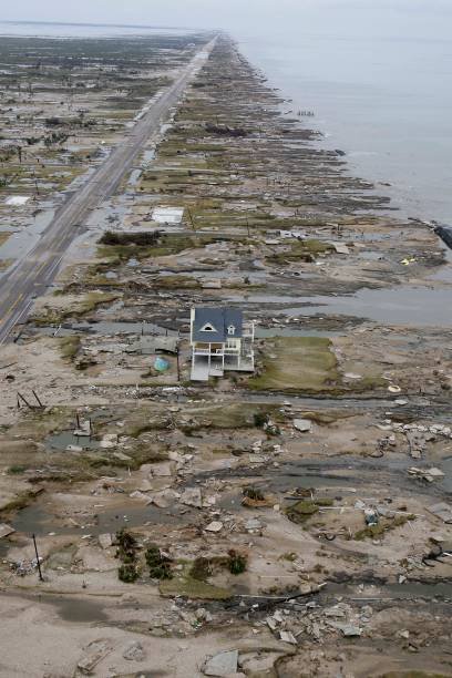 Aerial view of a coastline with widespread destruction, debris, and abandoned structures after a storm or disaster, with a house in the foreground.
