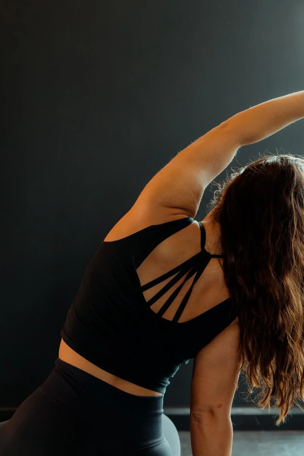 A female reformer pilates instructor wearing a black gym top and performing an overarm stretch.
