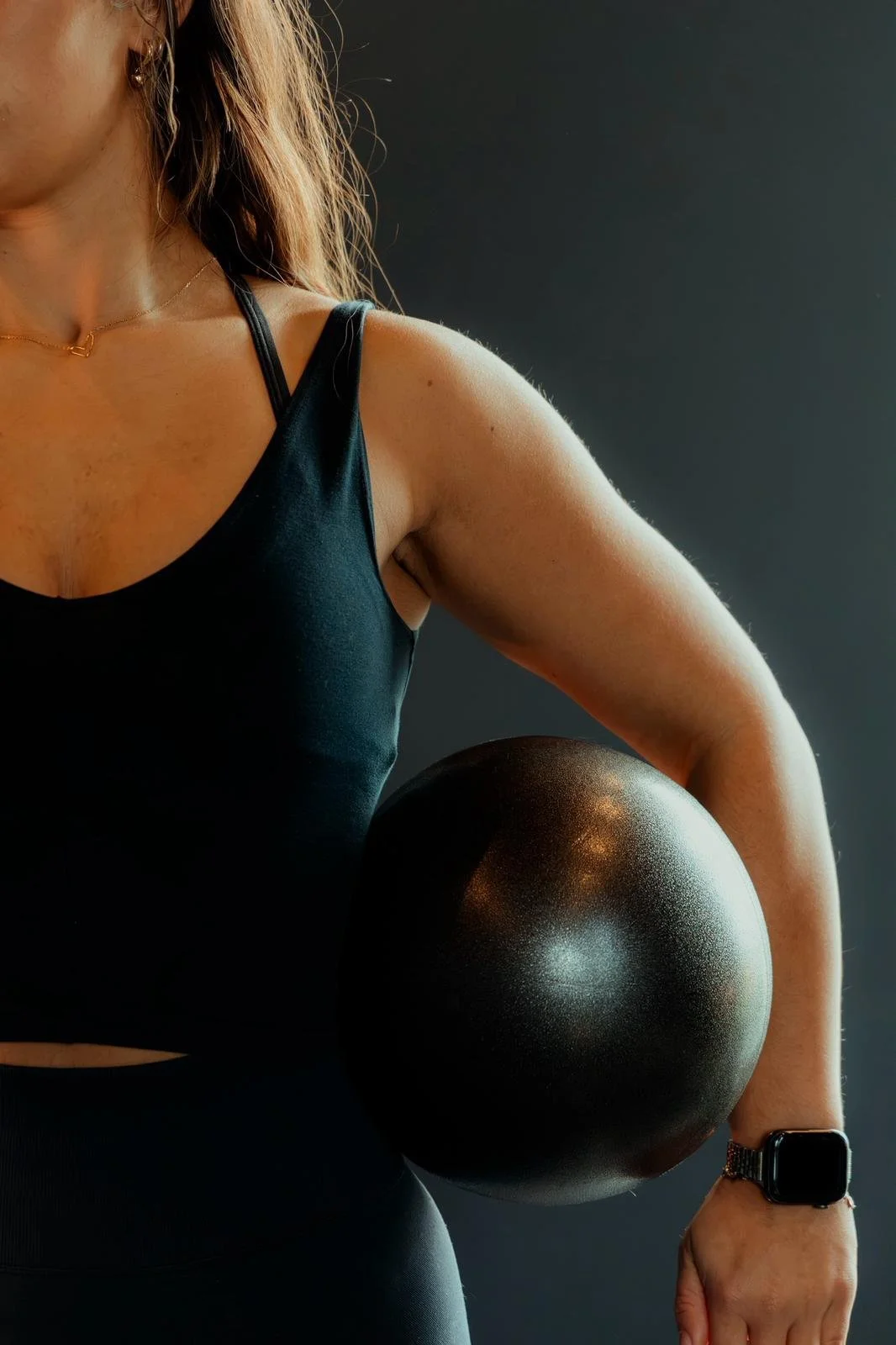 A cropped photo of a female reformer pilates instructor in black gym clothes is holding a pilates ball.