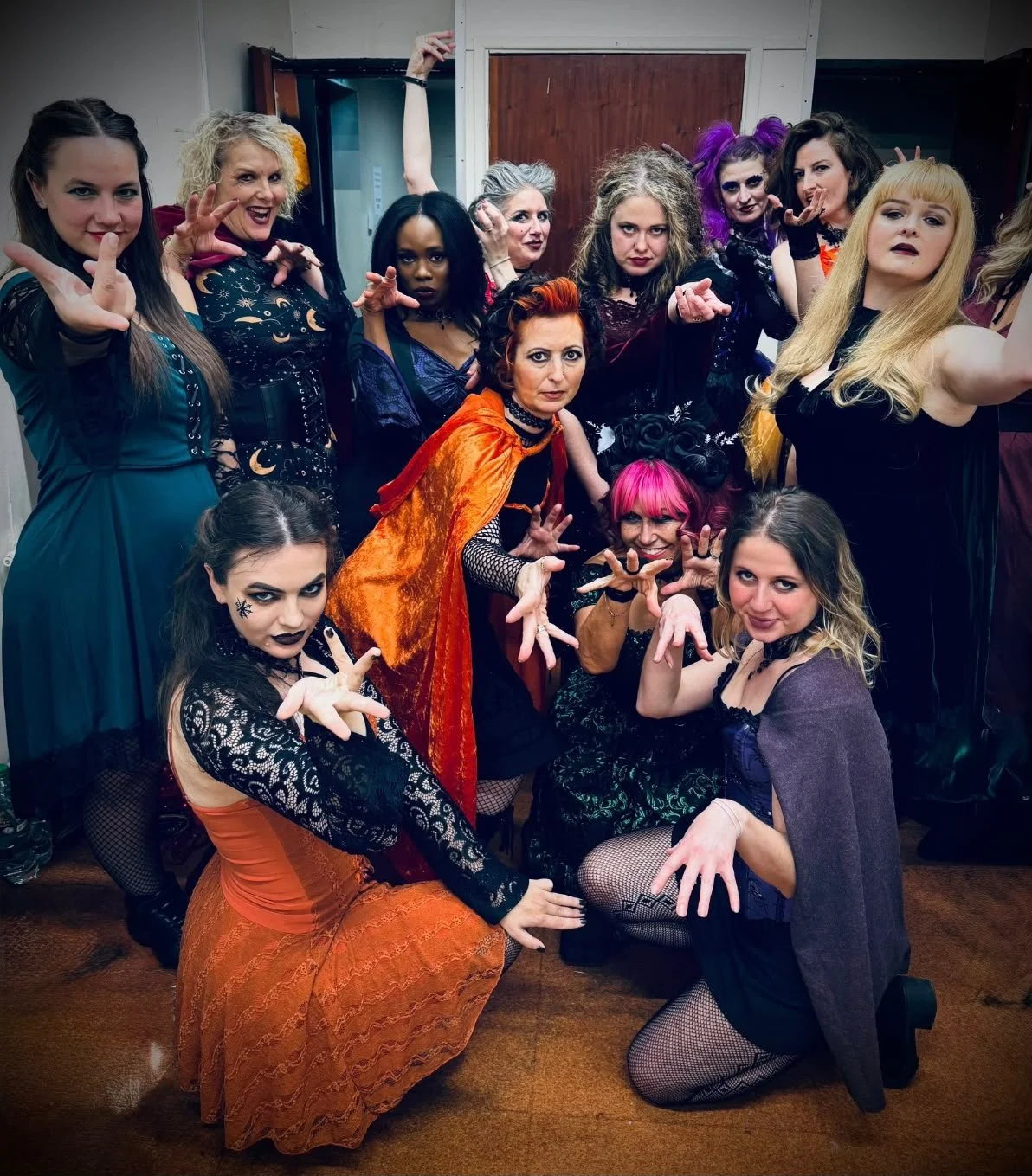 Group of women dressed in goth and Halloween costumes posing with spooky gestures in a room.