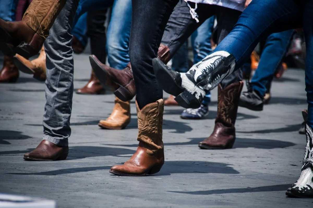 People wearing cowboy boots and jeans, demonstrating a line dance or similar activity outdoors.