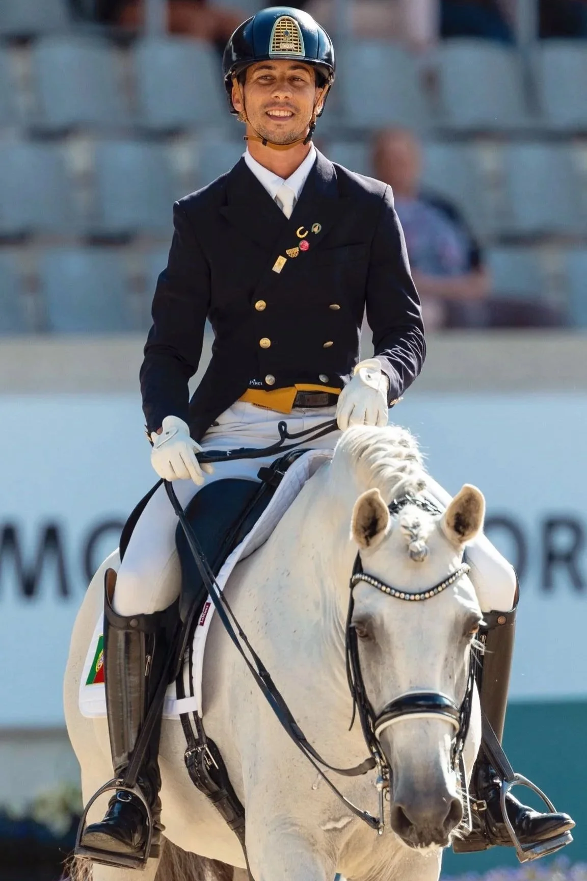 A man dressed in formal equestrian attire riding a white horse during a dressage event.