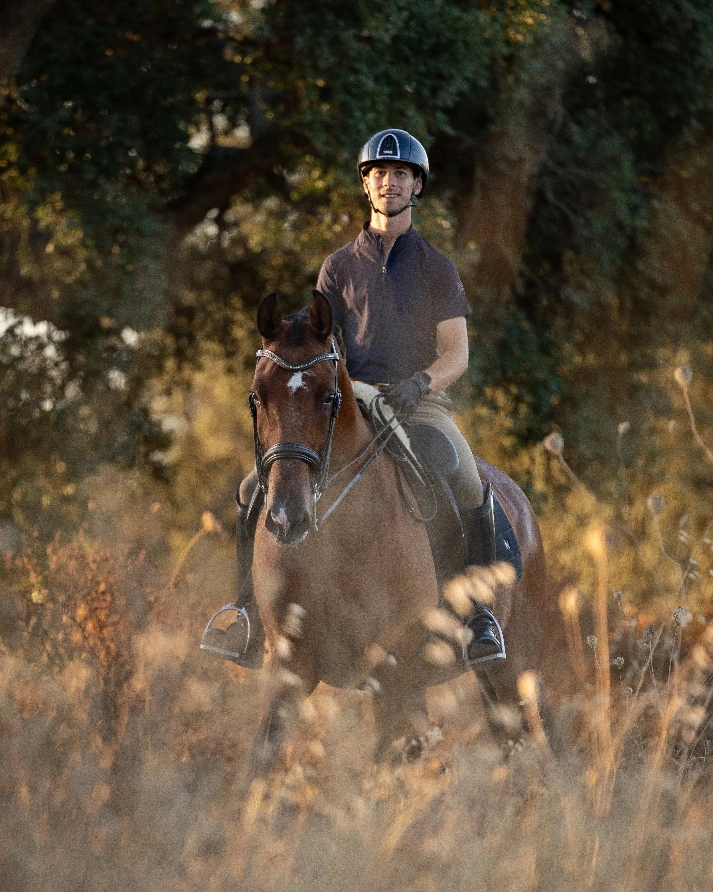 A man riding a brown horse through a field during sunset.