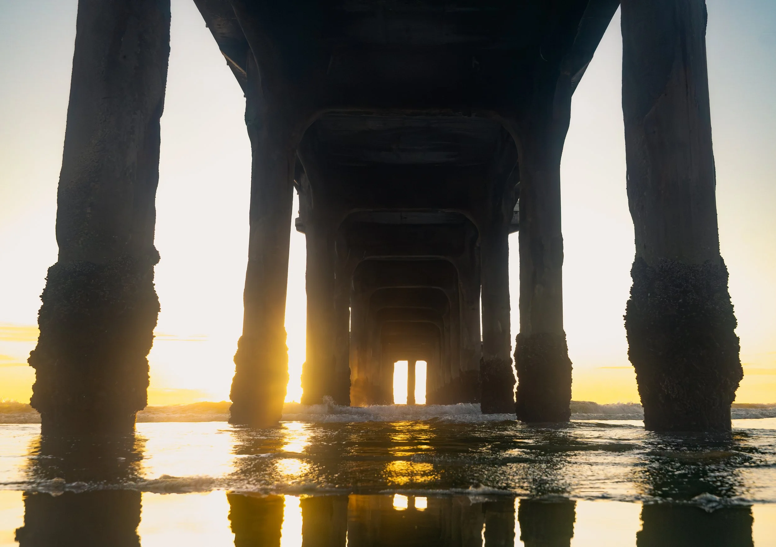 Minimal photograph of pier columns at sunset with reflected light on wet sand