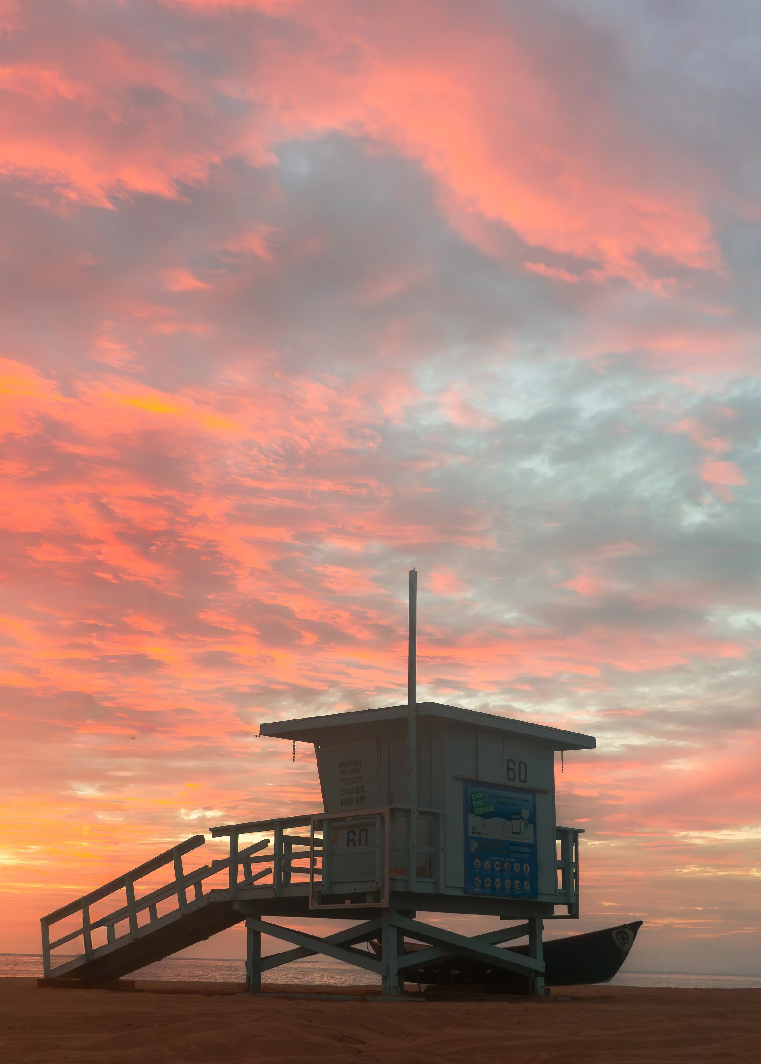 A lifeguard tower on a beach at sunrise or sunset, with pink and orange clouds in the sky.