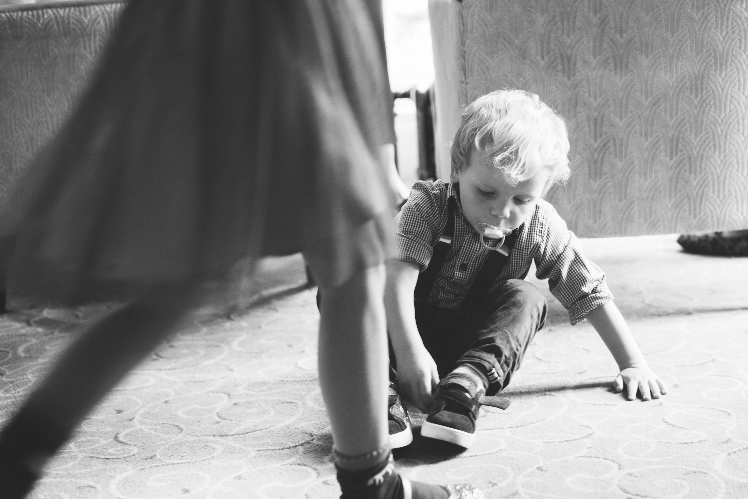 A young boy playing quietly on the floor near his mother’s legs, capturing an early moment of safety, closeness, and embodied connection.