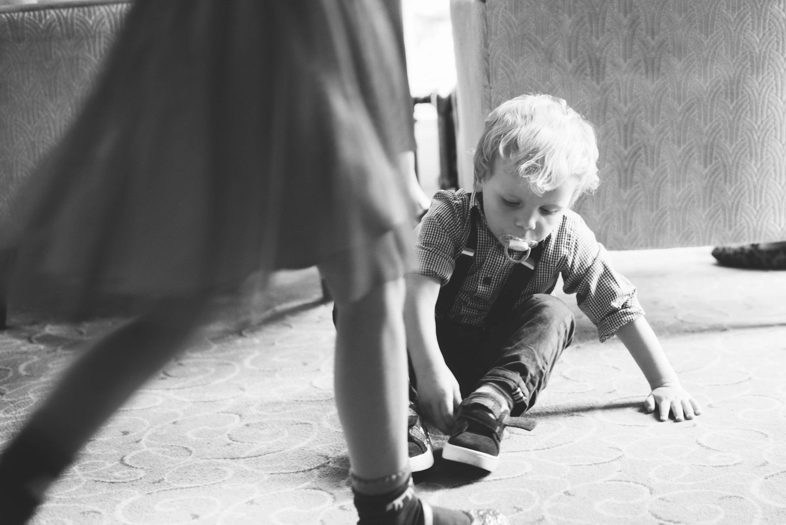 A young boy playing quietly on the floor near his mother’s legs, capturing an early moment of safety, closeness, and embodied connection.