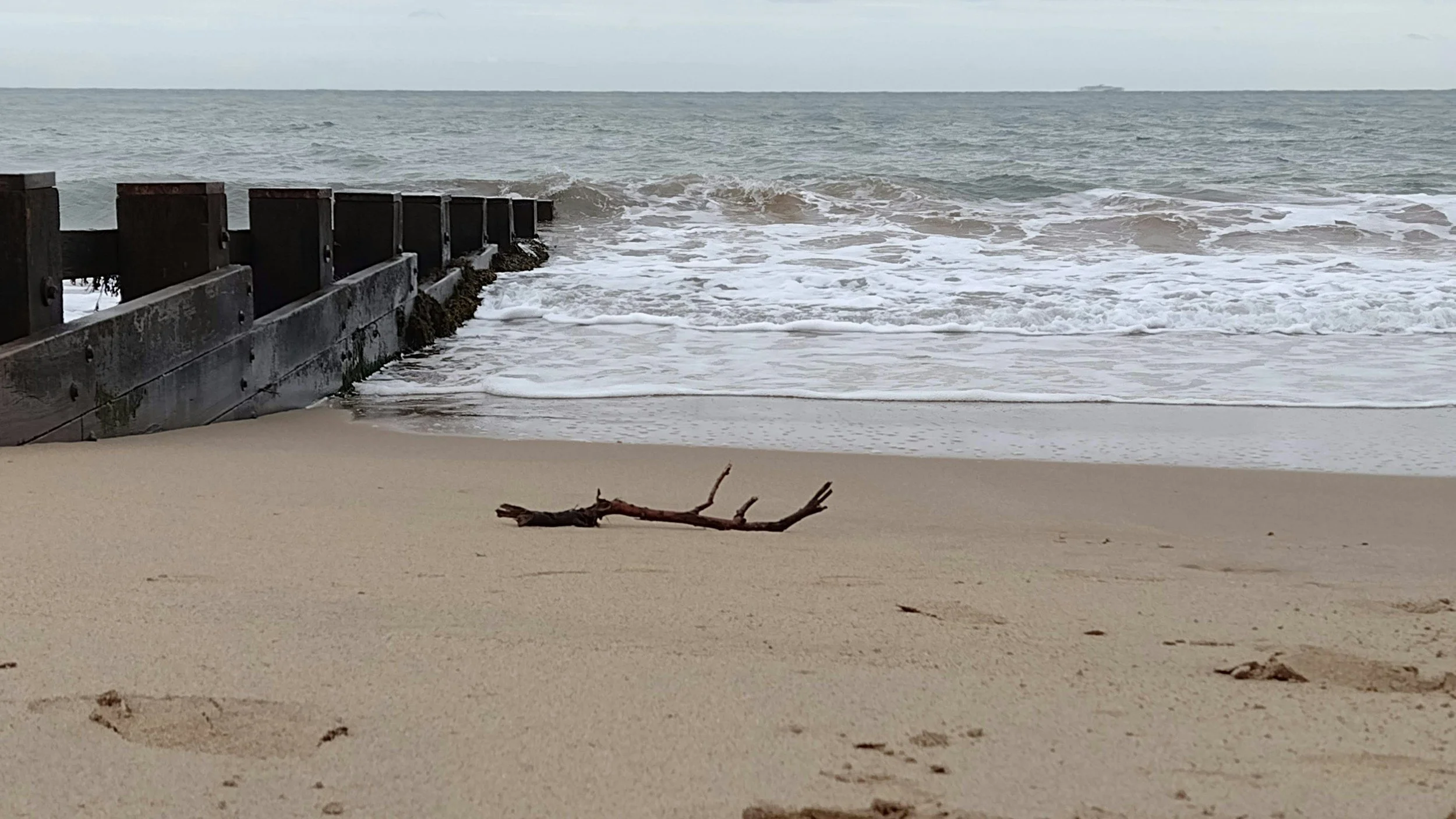 Concrete breakwater holding back strong waves under an overcast sky, symbolising emotional capacity and anxiety tolerance in therapy.