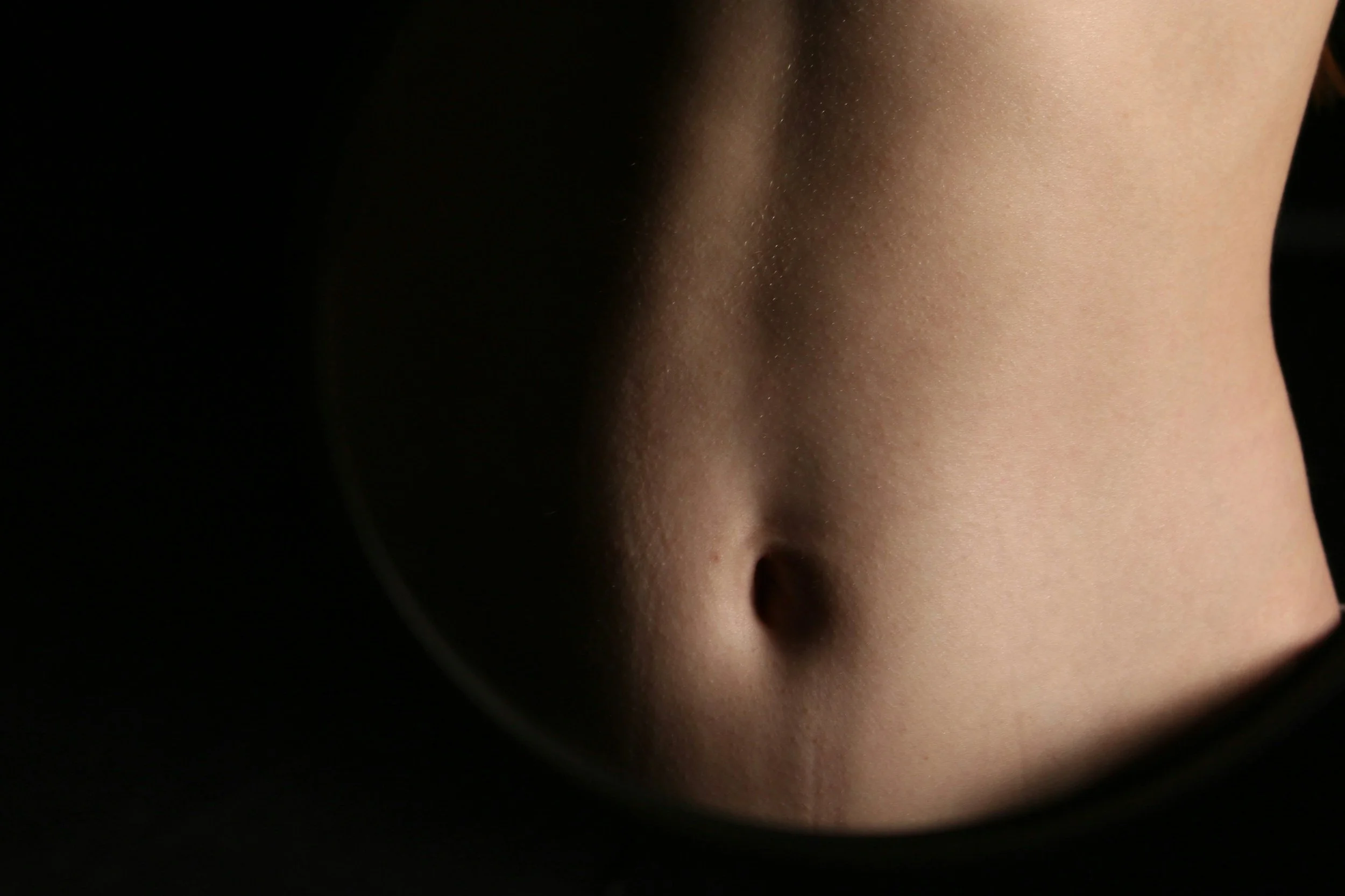 Close-up of a human abdomen in soft light, representing how core emotions begin as bodily activation in the gut.