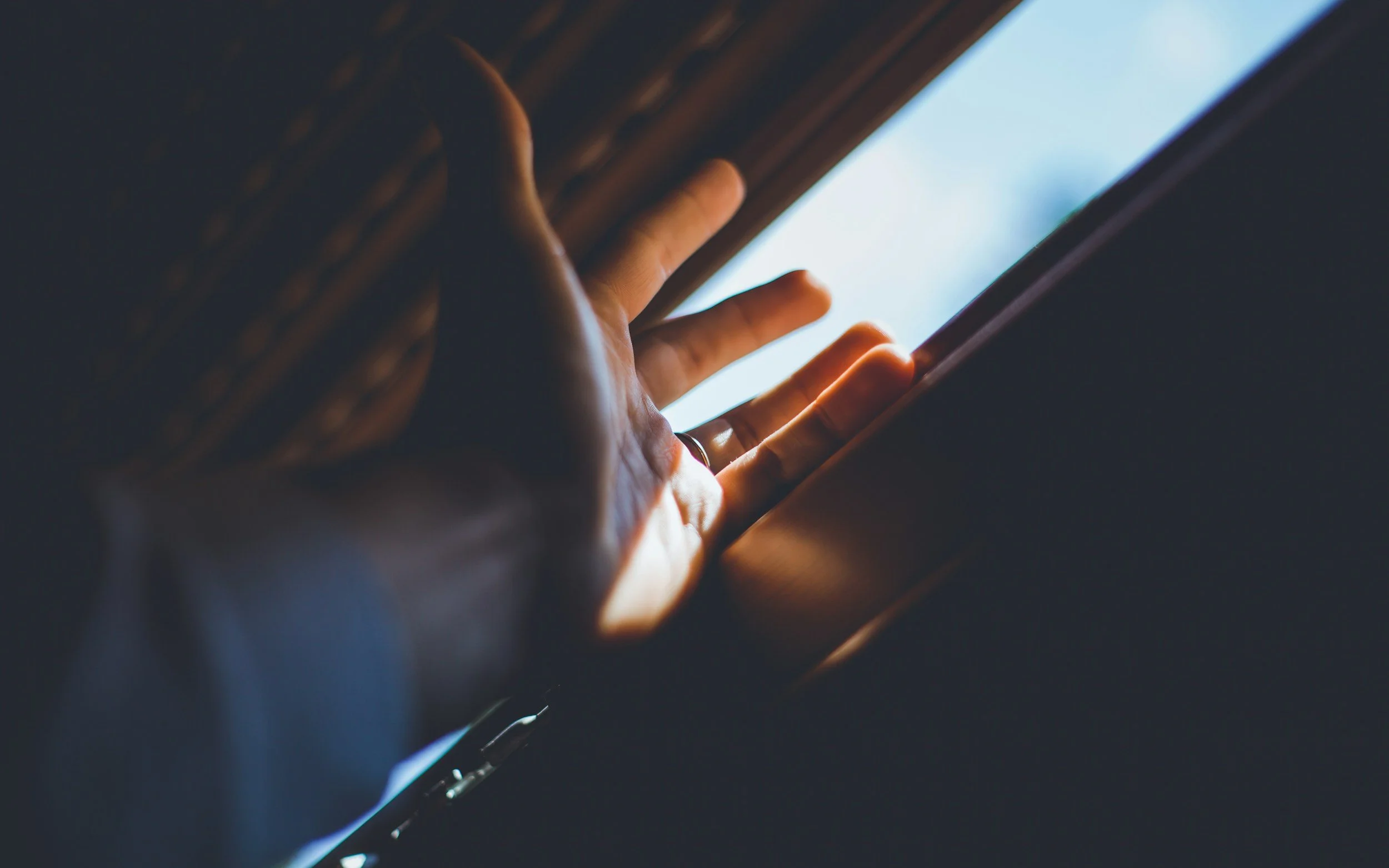 Hand reaching toward light through a window, symbolising emotional numbness and the experience of feeling distant from one's emotions