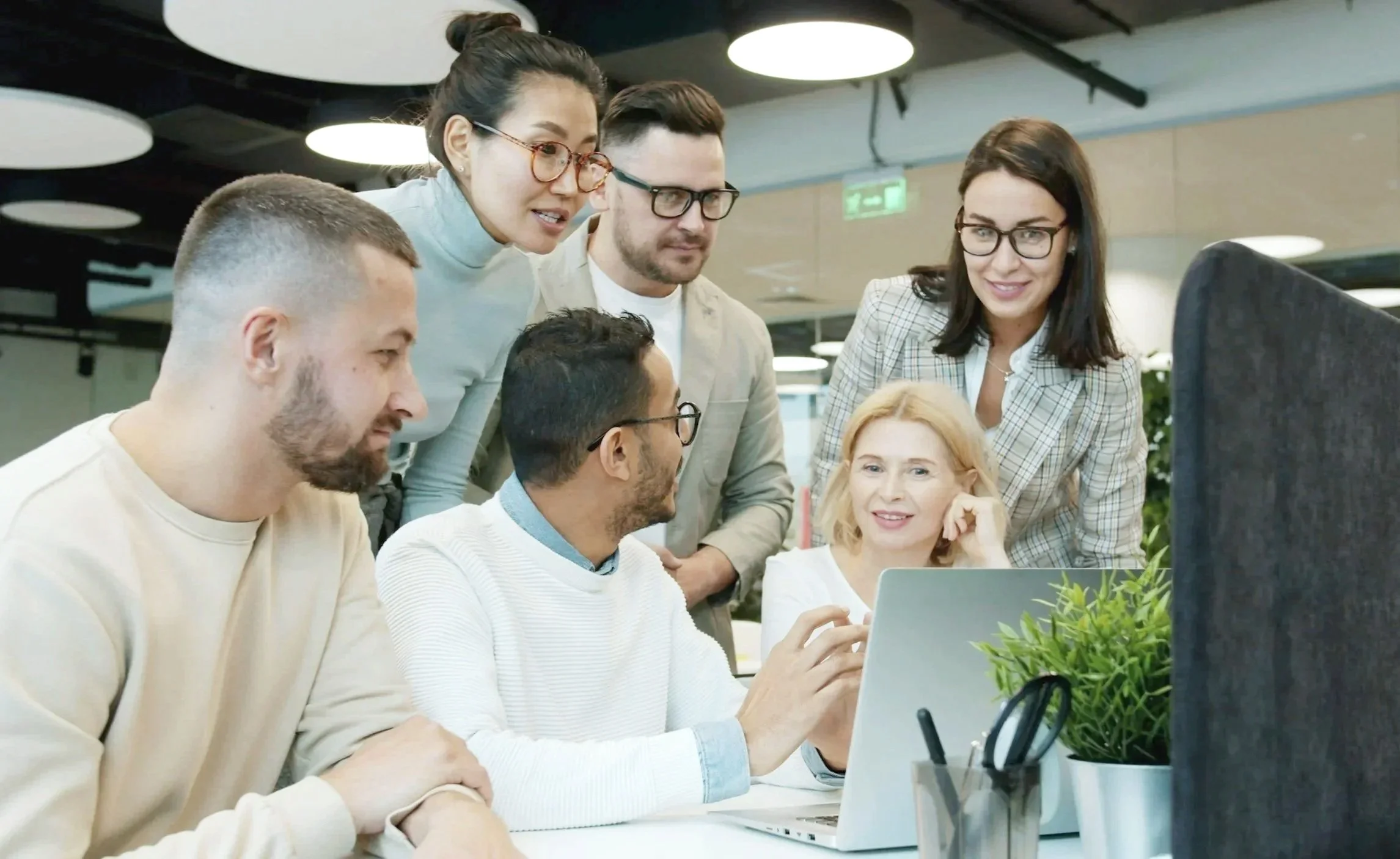 Three business men and three business women gathered around a laptop and smiling