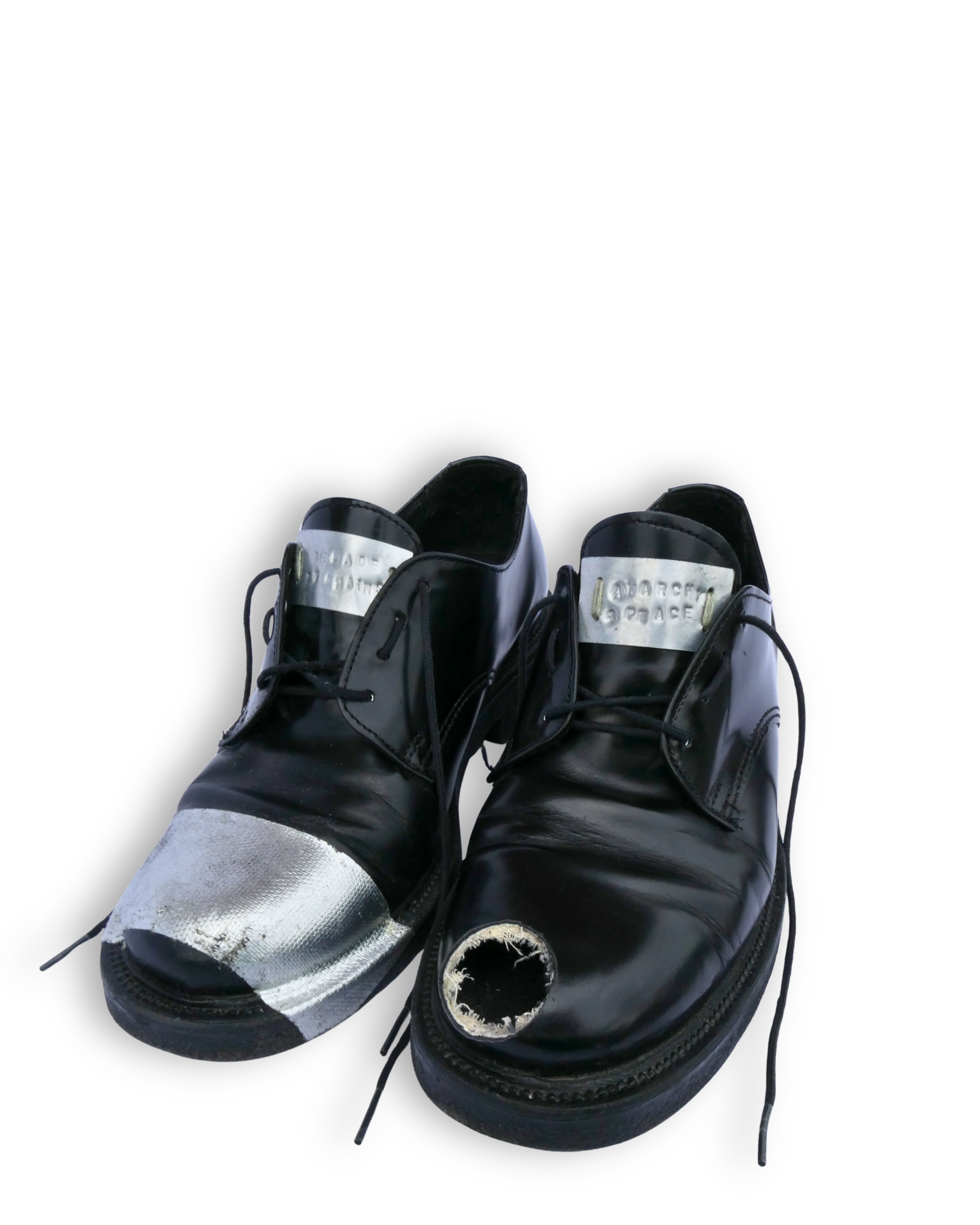 Pair of black leather dress shoes with paint damage on the toes, one shoe has a large hole near the toe, and the other has a patch of silver paint.