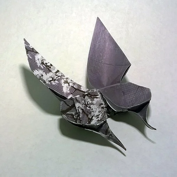 Purple and white origami butterfly with floral patterned wings on a white surface.