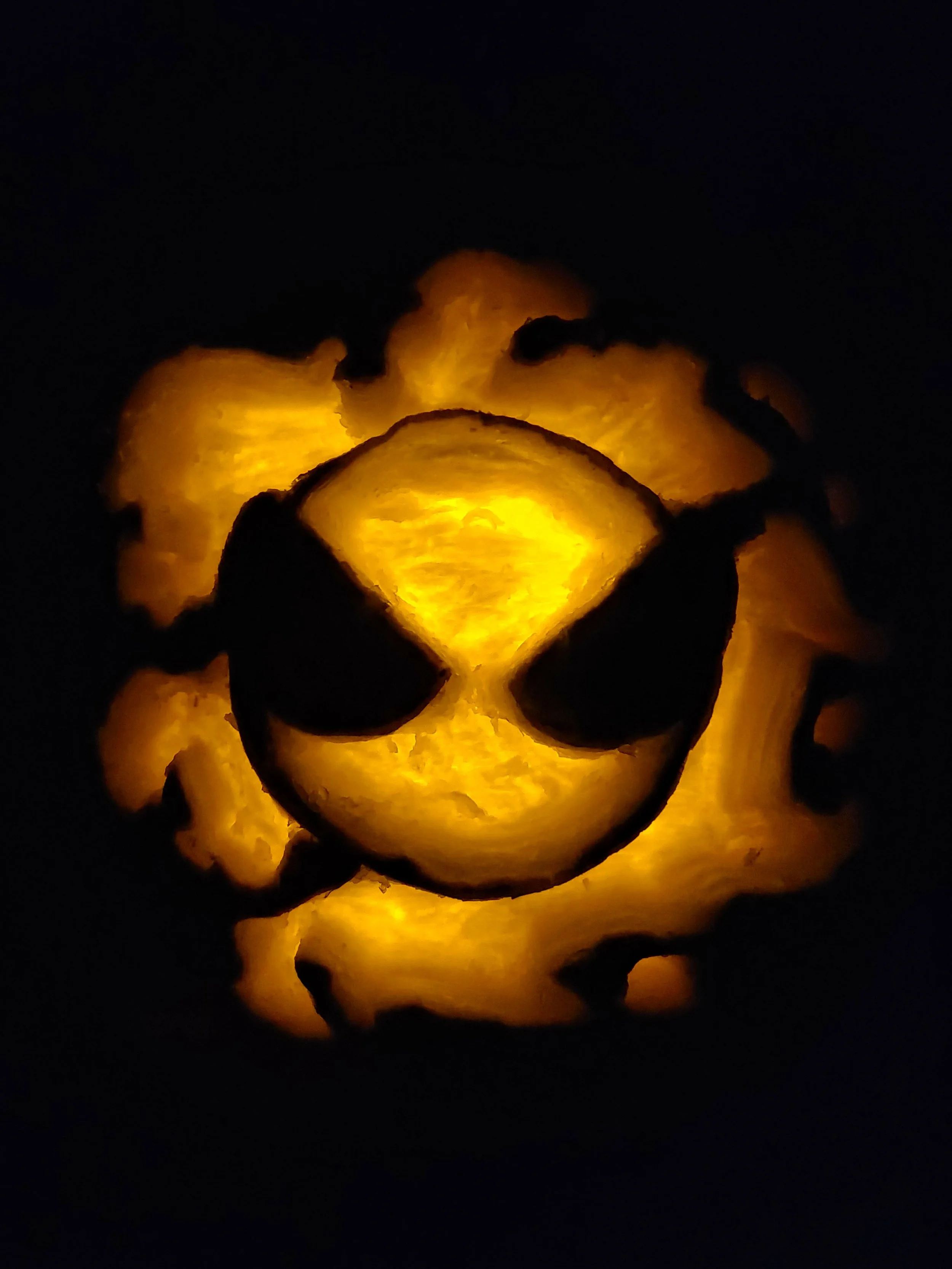 A carved pumpkin of Gastly from Pokémon, illuminated from inside against a dark background.