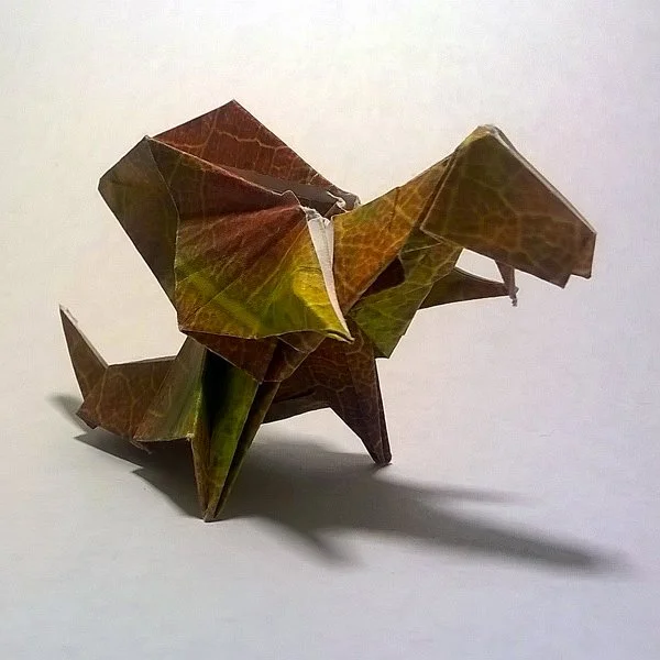 Origami dragon made from paper with a leaf pattern, standing on a white surface.
