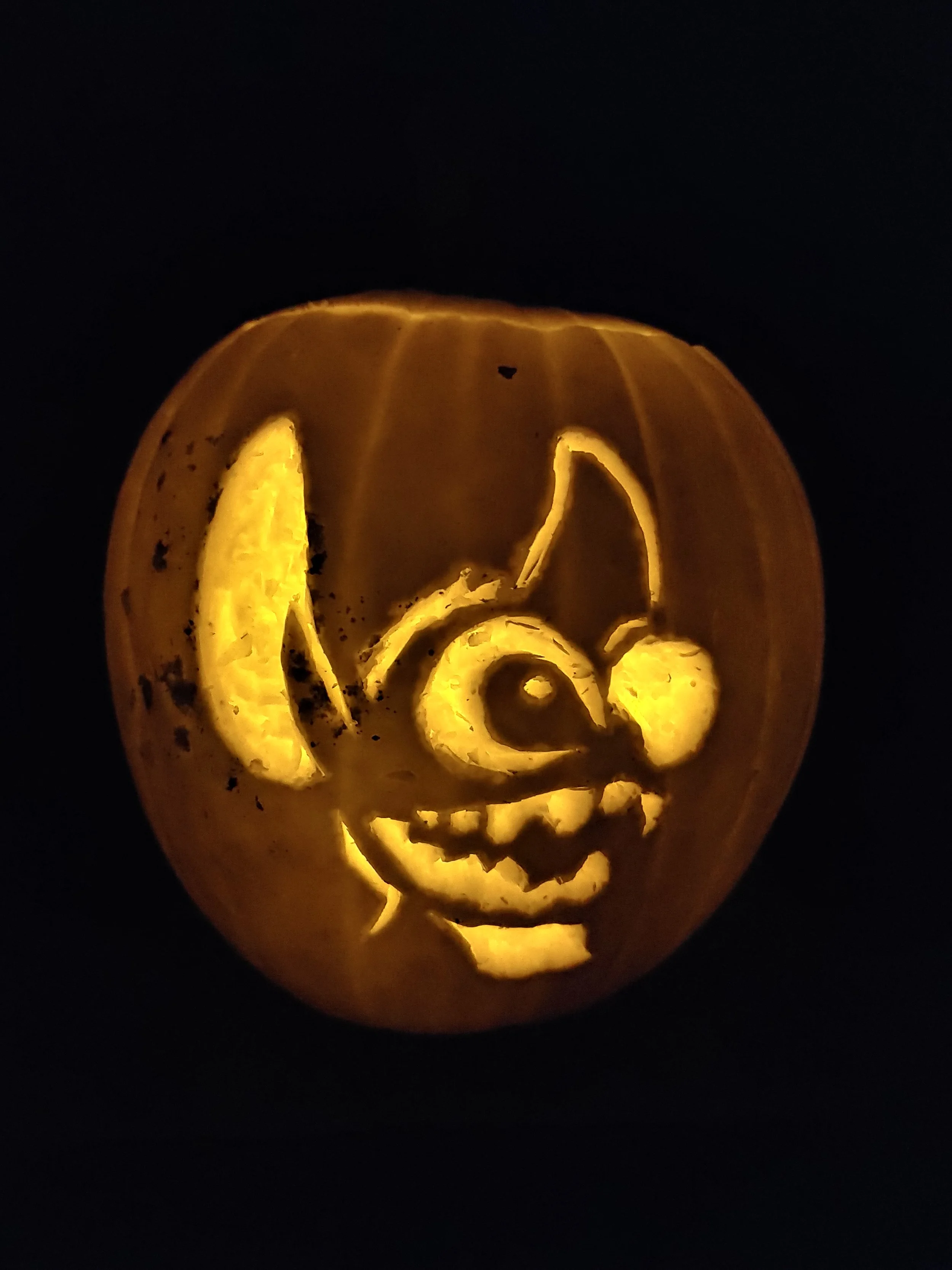 A carved pumpkin of Stitch from Lilo & Stitch, illuminated from inside against a black background.