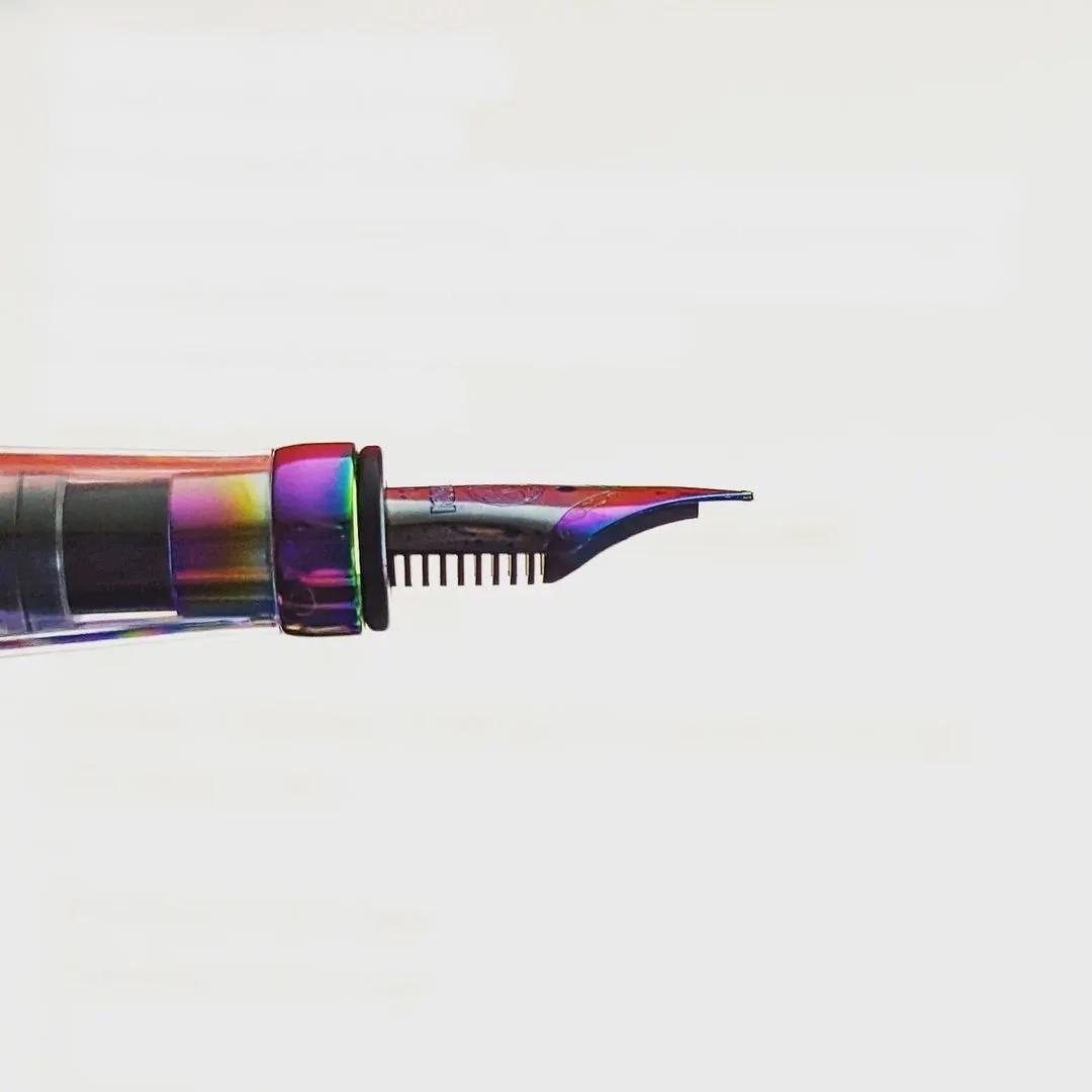 Close-up of a colorful TWSBI 580 Iris fountain pen nib with a transparent barrel, set against a plain white background.