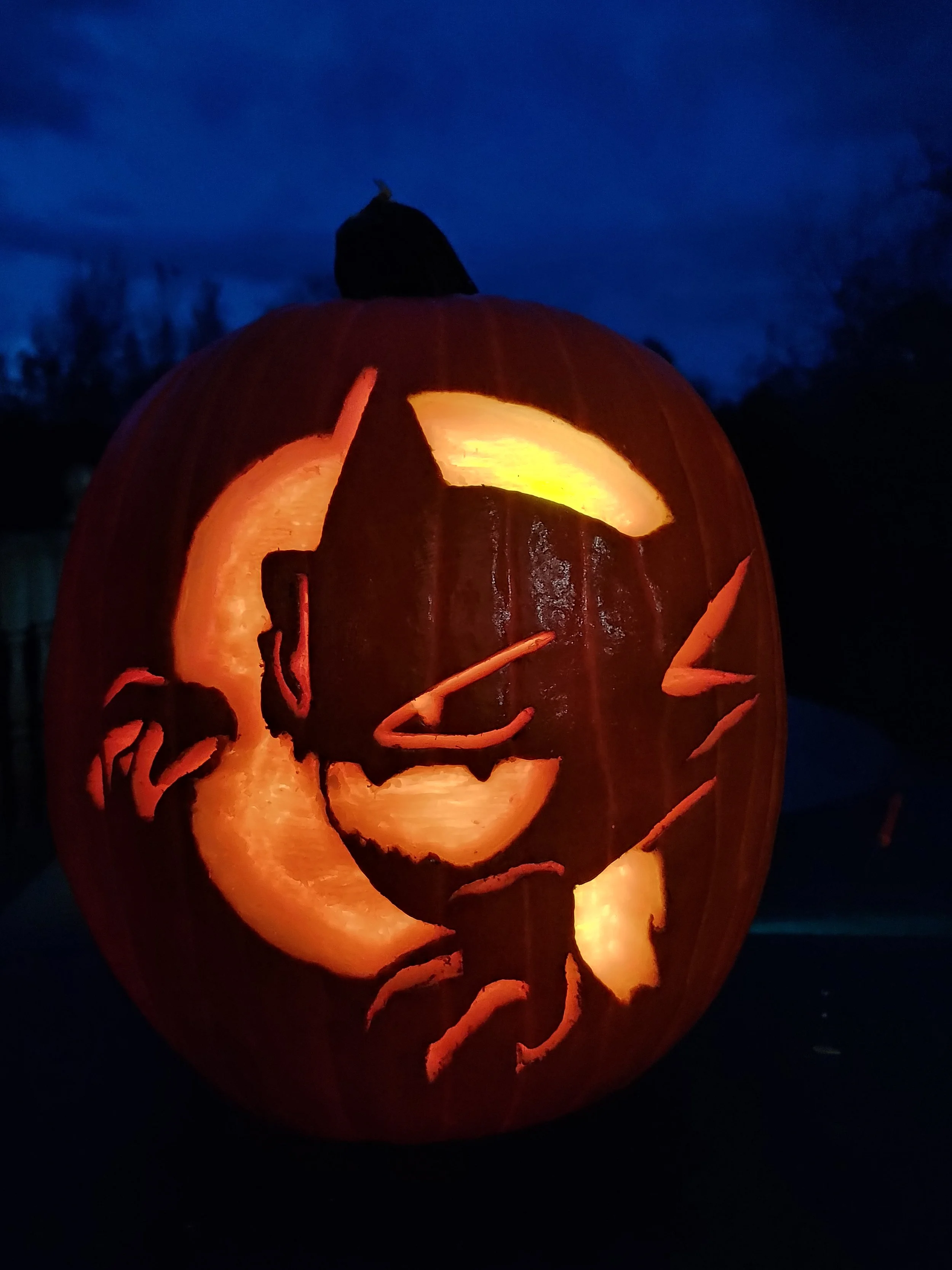 Carved pumpkin of Haunter from Pokémon, illuminated from inside, against a dark outdoor background at night.