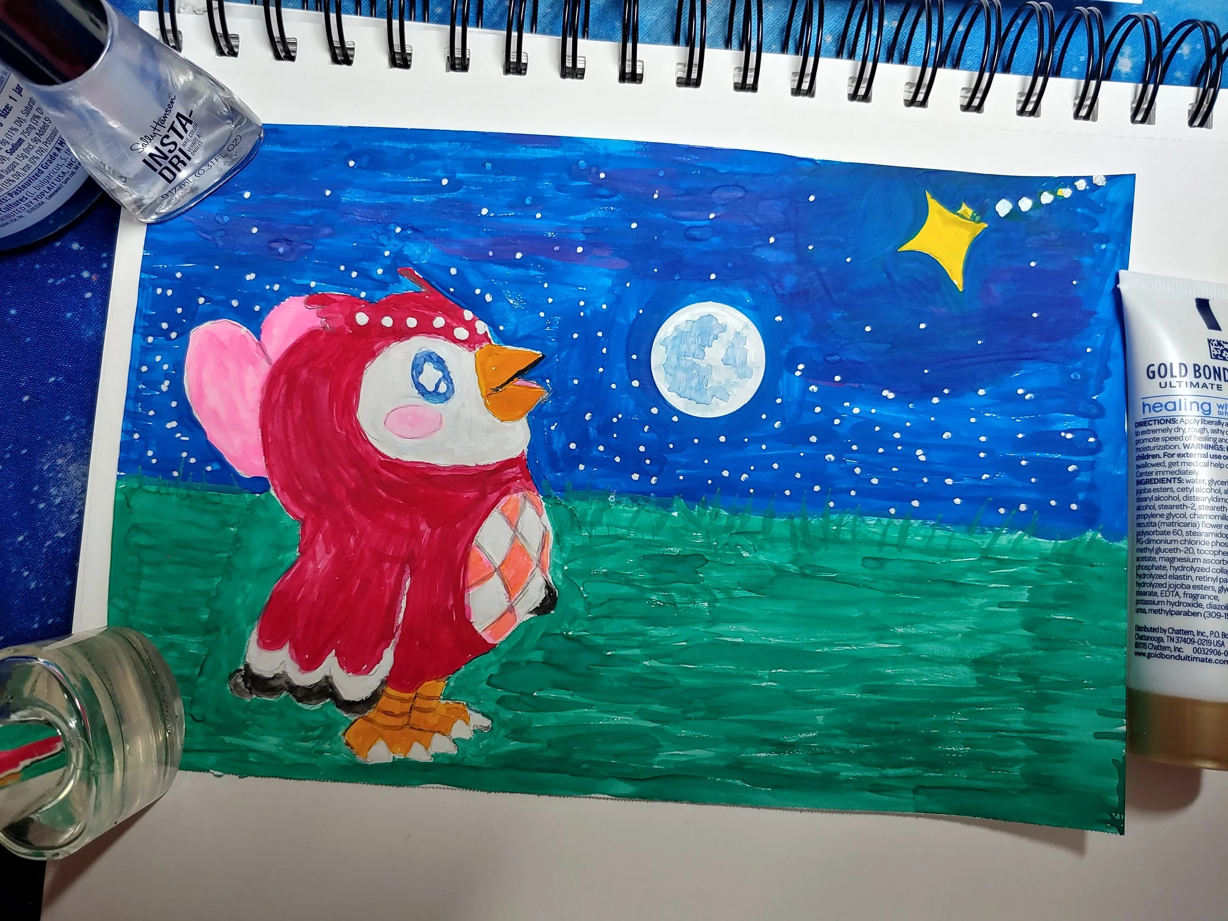 A colorful drawing of a pink and white bird with a yellow beak and orange feet, standing on a green surface under a night sky with a full moon and a yellow star, painted on a piece of paper with supplies around it.