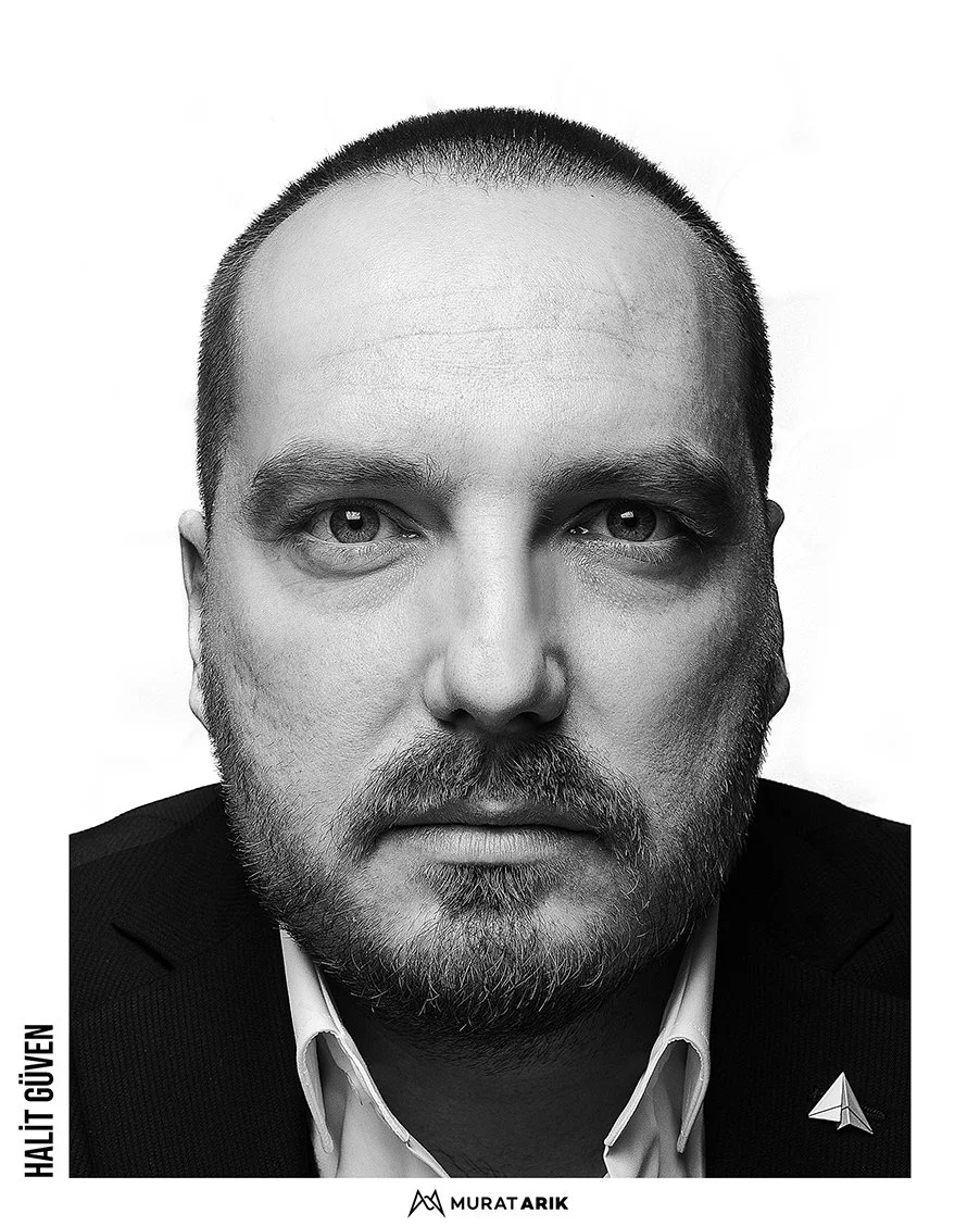 Black and white portrait of a man with short hair and a beard, wearing a suit jacket with a Star Trek communicator badge, looking directly at the camera.