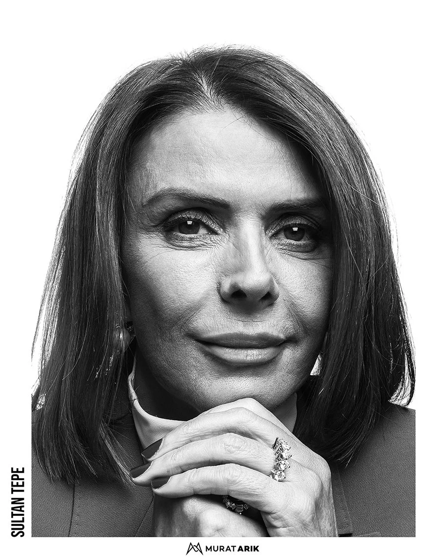 Close-up black and white portrait of a woman with shoulder-length hair, wearing jewelry, resting her chin on her hand.