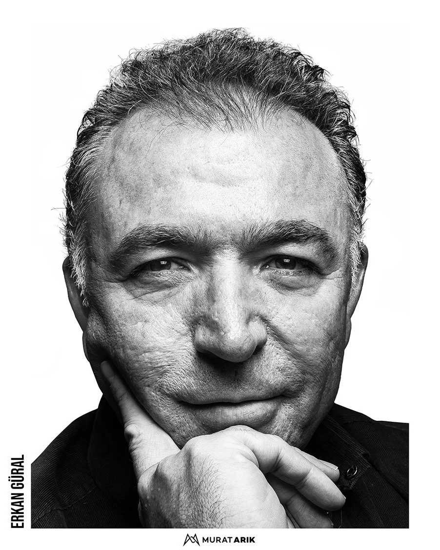 Black and white close-up portrait of Erkan Güral with short hair, resting his chin on his hand, looking thoughtfully into the camera.