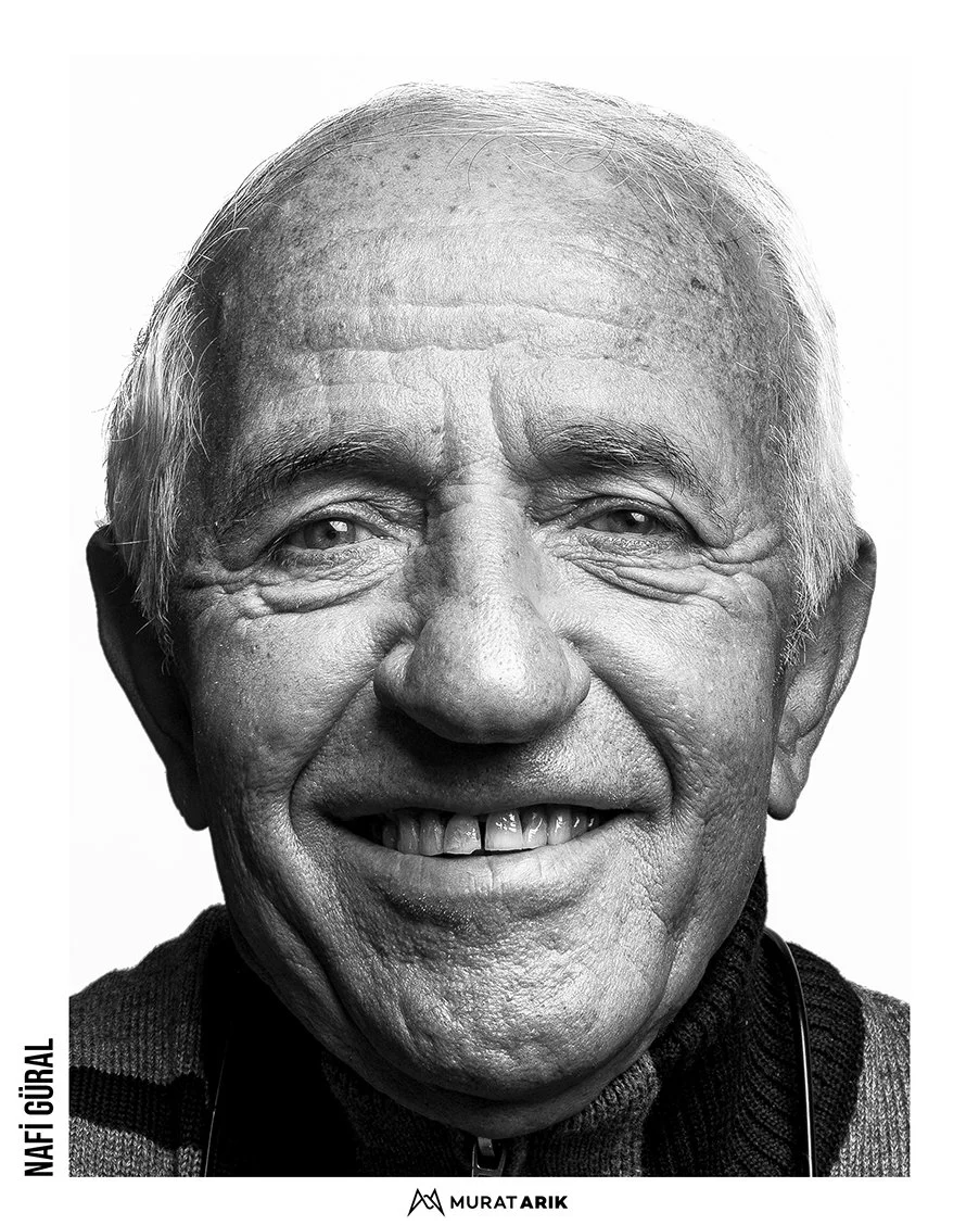 Close-up black and white portrait of an elderly man smiling, showing teeth, with deep wrinkles and short white hair.