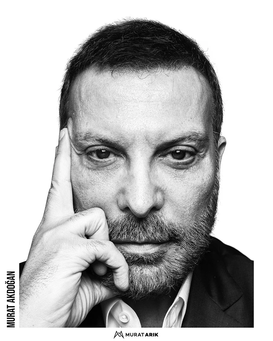 Black and white portrait of a man with short hair and a beard, wearing a suit and white shirt, resting his face on his hand.