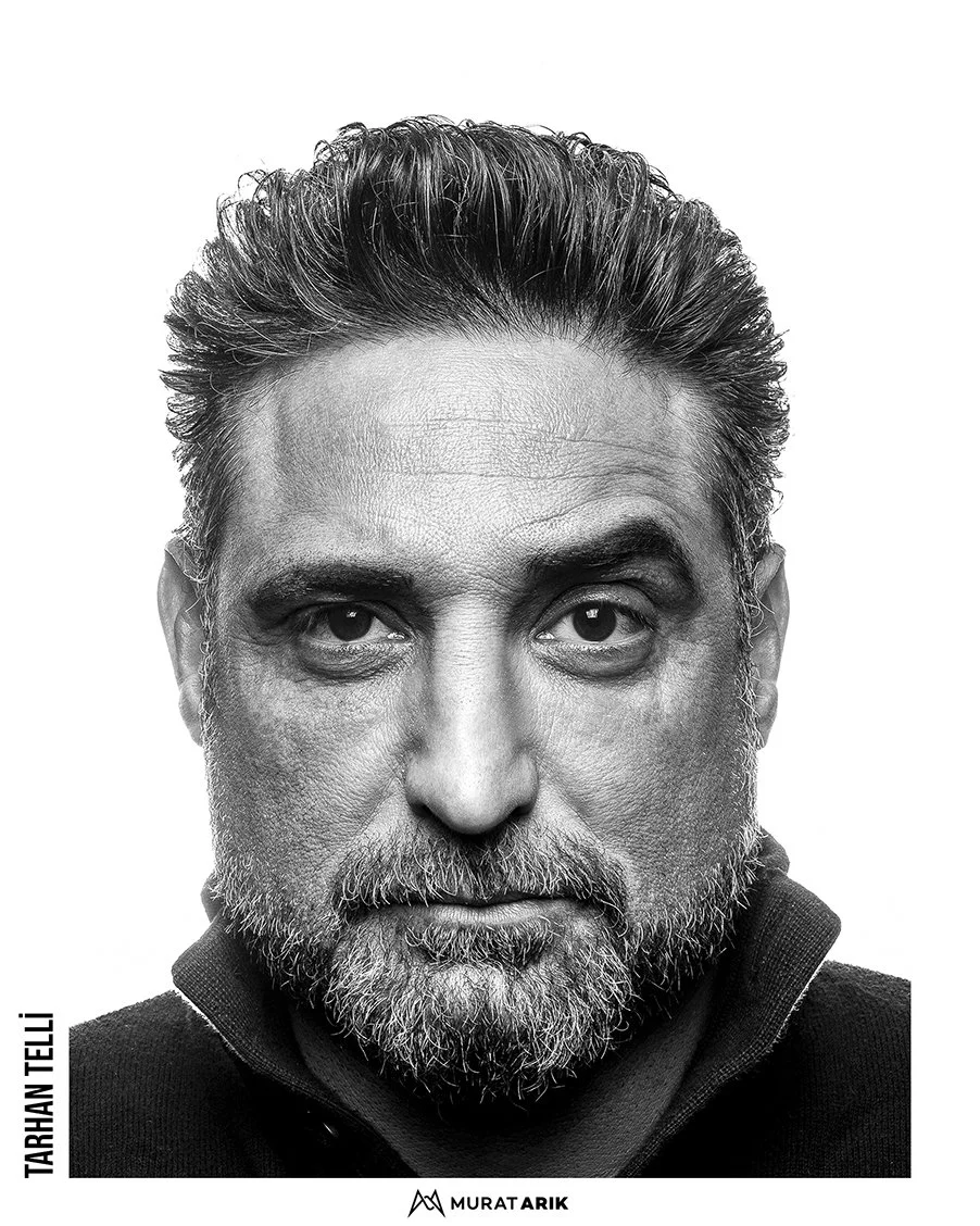 Black and white portrait of a middle-aged man with styled hair and a beard, wearing a dark zip-up jacket.